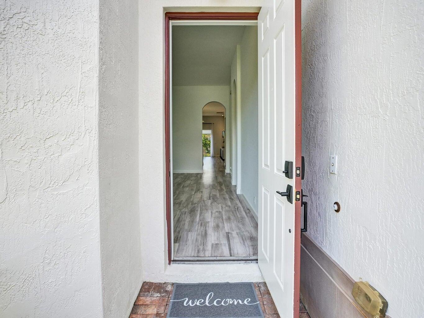 Open front door reveals a long hallway with gray tile flooring and an arched opening.