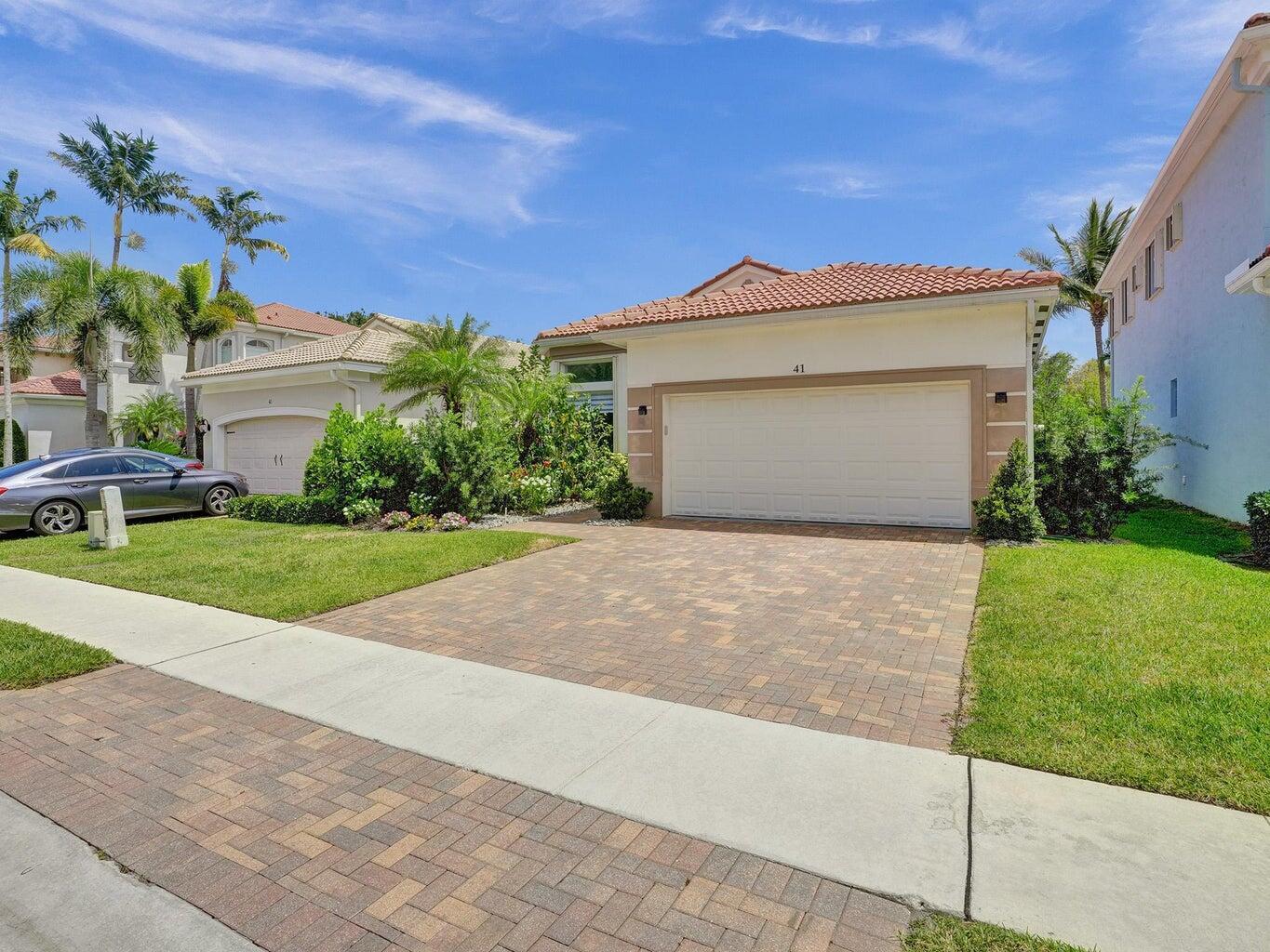 Home with a terracotta tile roof, two-car garage, paver driveway, and landscaped front yard.
