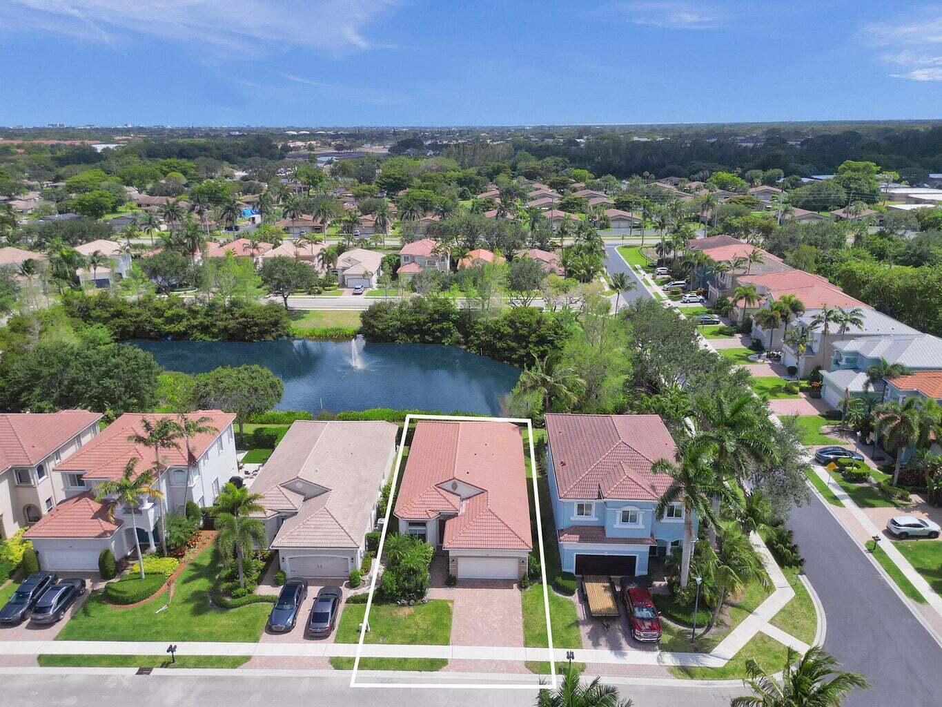 Aerial view of a home outlined beside a pond with a fountain in a palm-lined neighborhood.