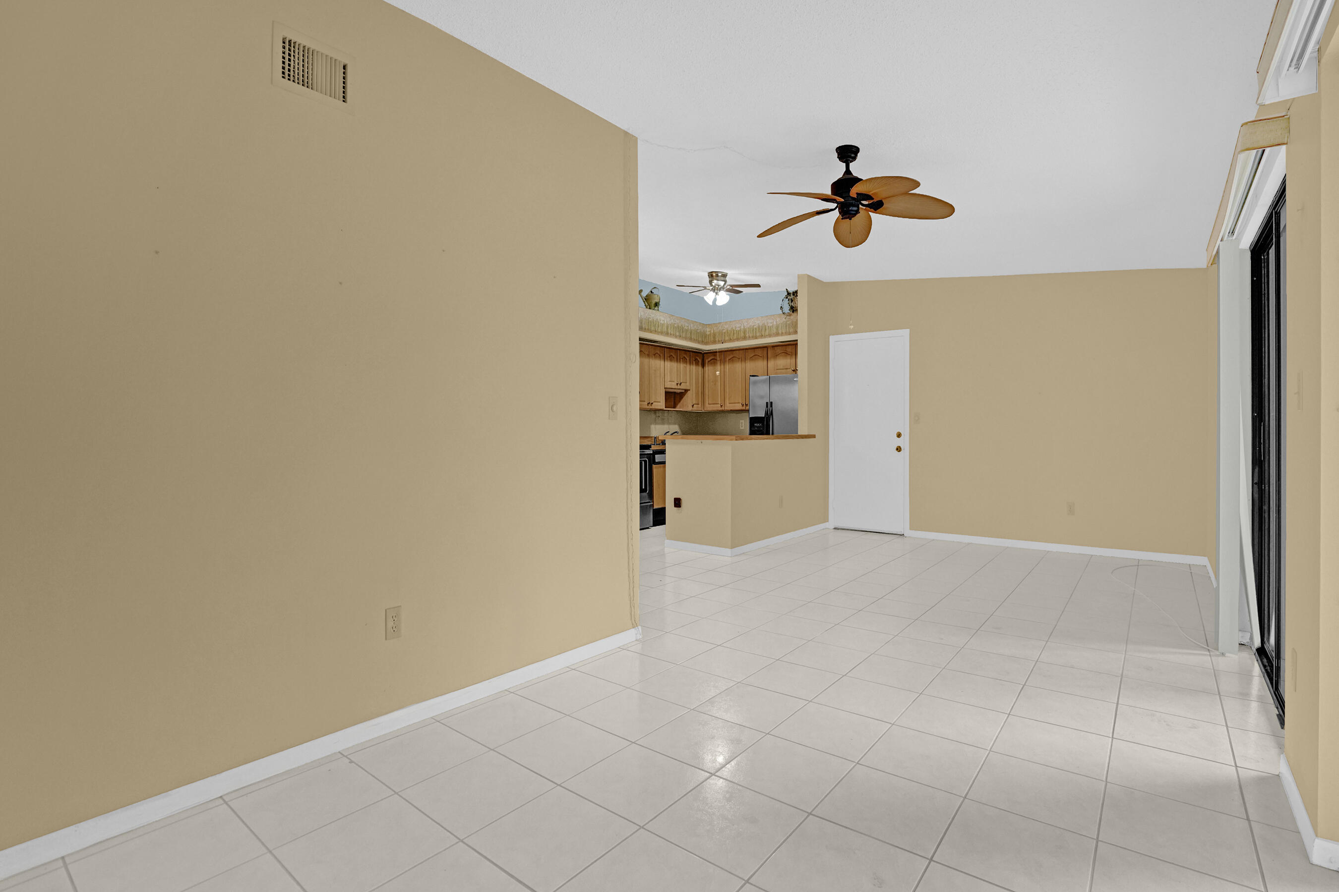 Empty tiled living area opening to a wood-cabinet kitchen, with two ceiling fans and sliding glass doors.