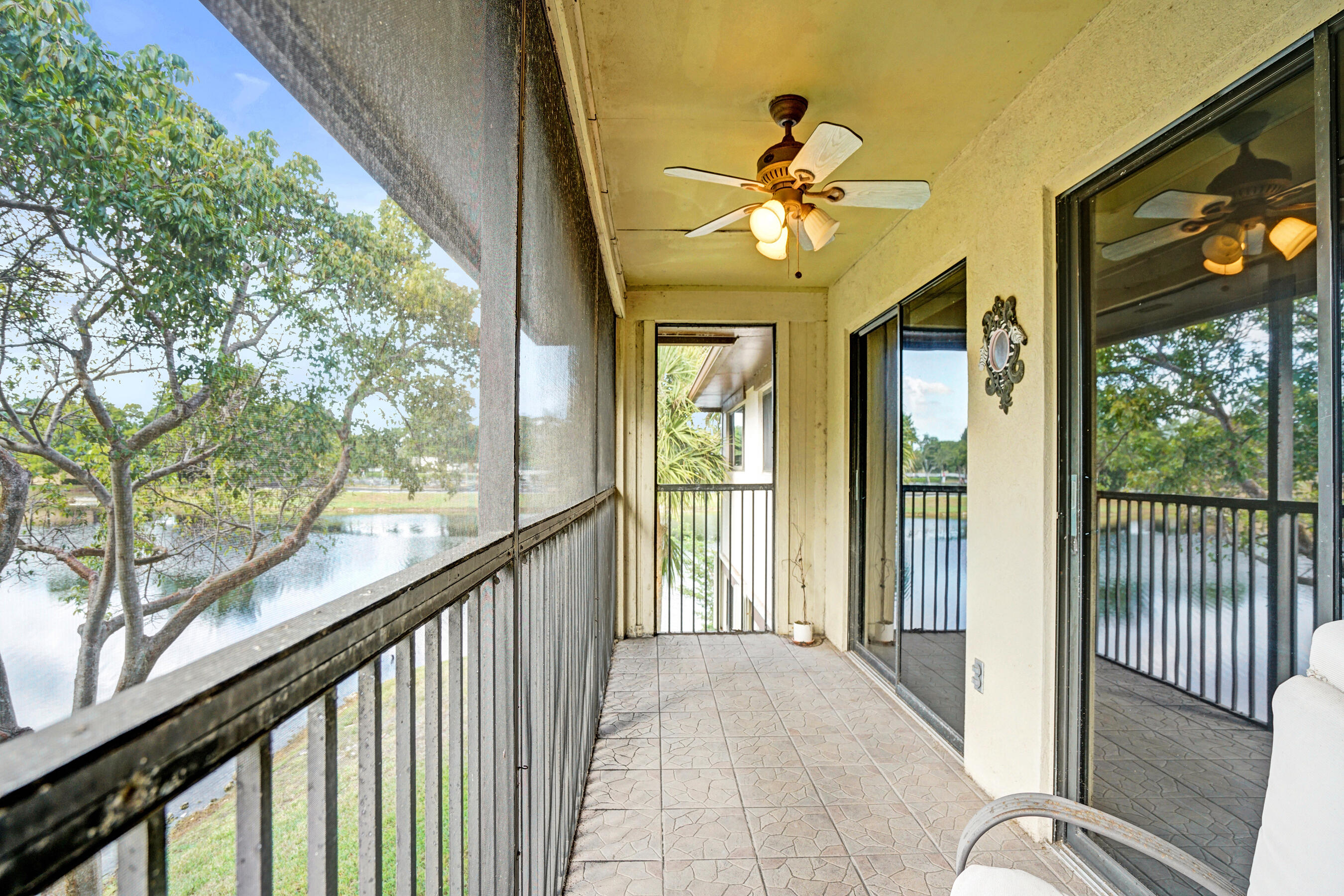 Screened condo balcony with tiled floor and ceiling fan overlooking a pond and trees.