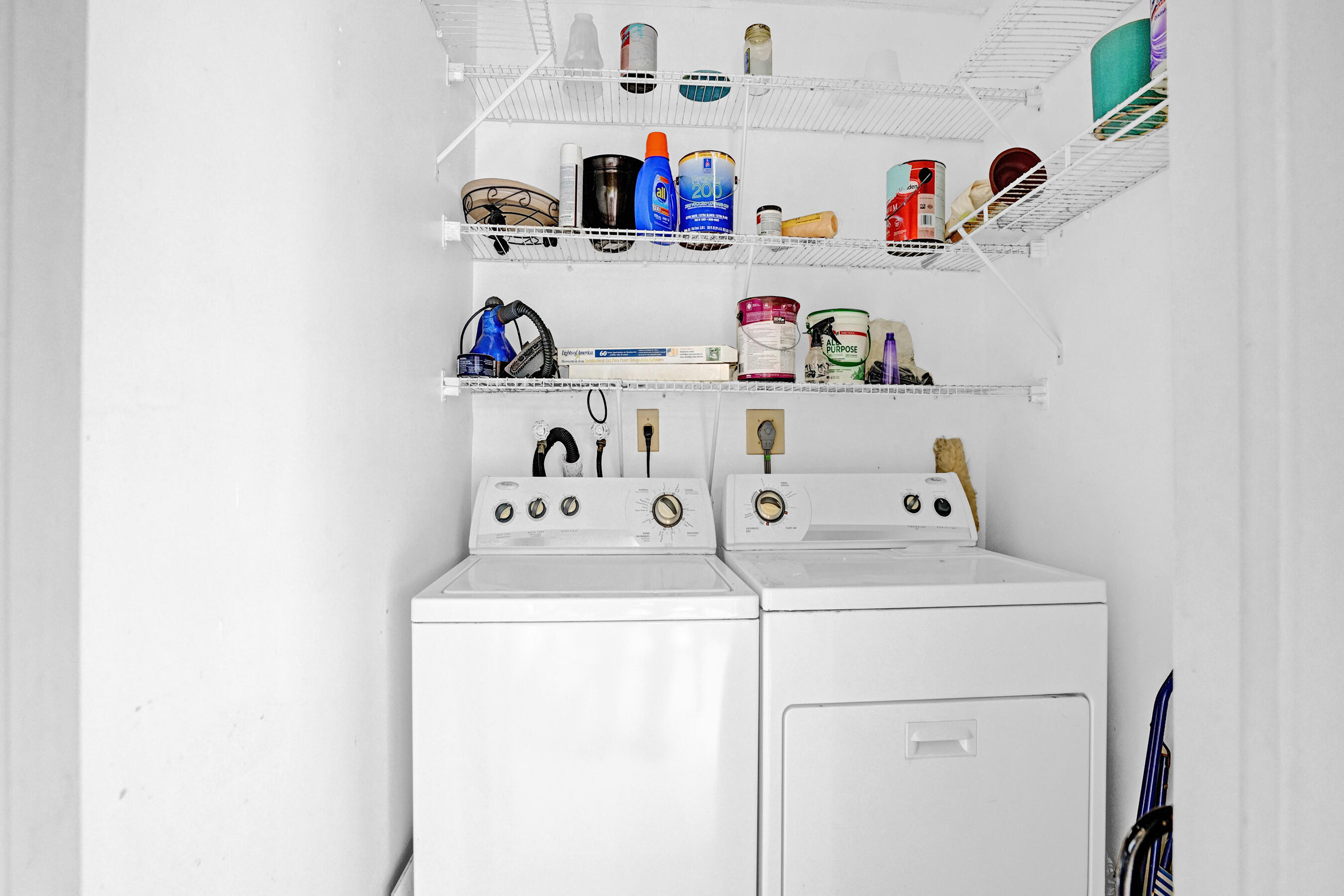 Laundry room with a washer and dryer beneath wire shelves stocked with cleaning supplies.