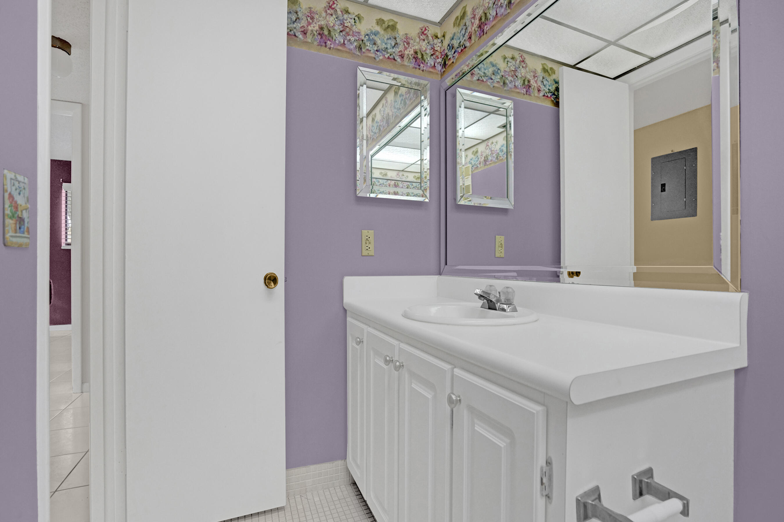 Bathroom with a long white vanity and mirrored wall, lavender paint, and floral ceiling border.