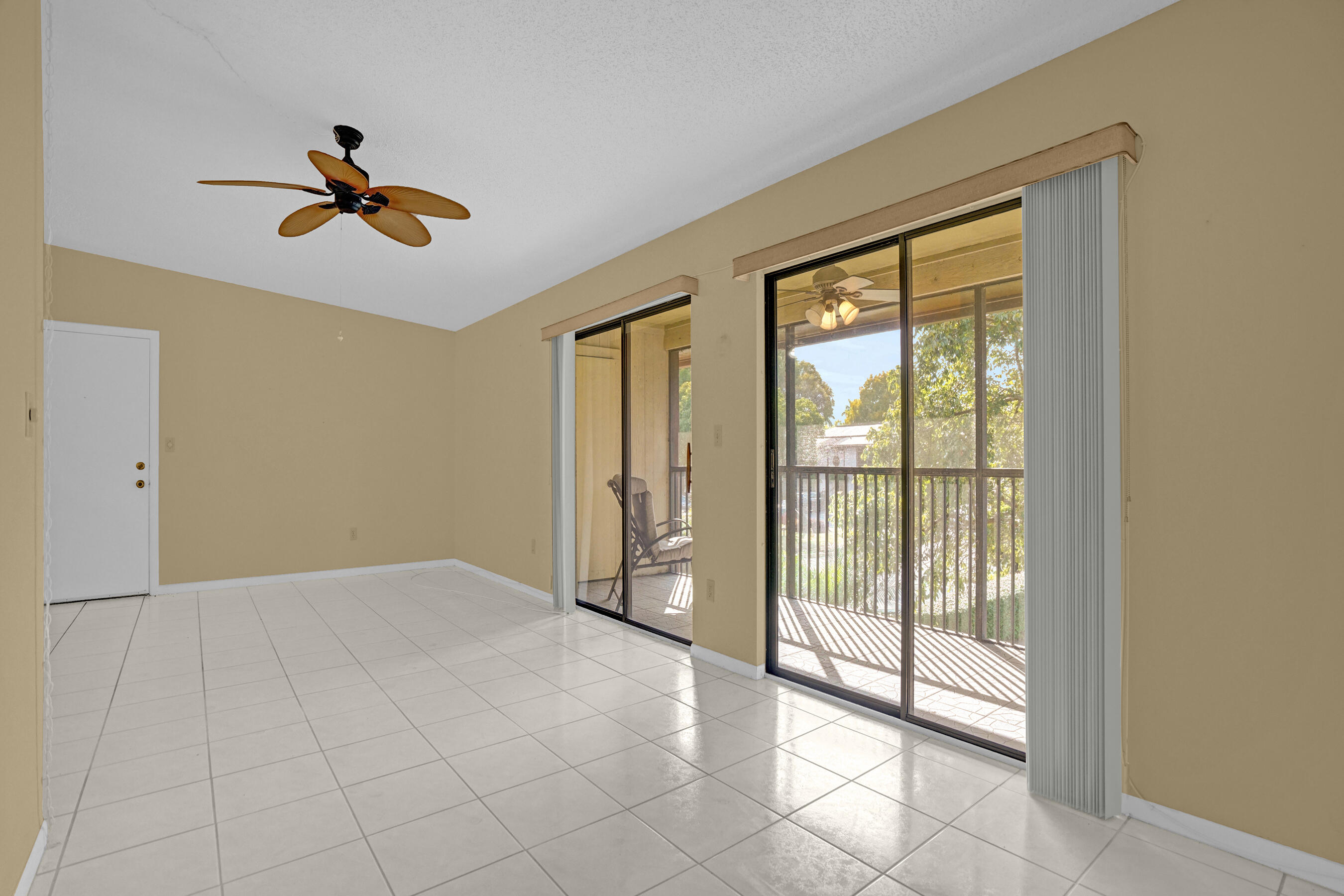 Empty living room with tiled floors, ceiling fan, and sliding doors to a sunny balcony.
