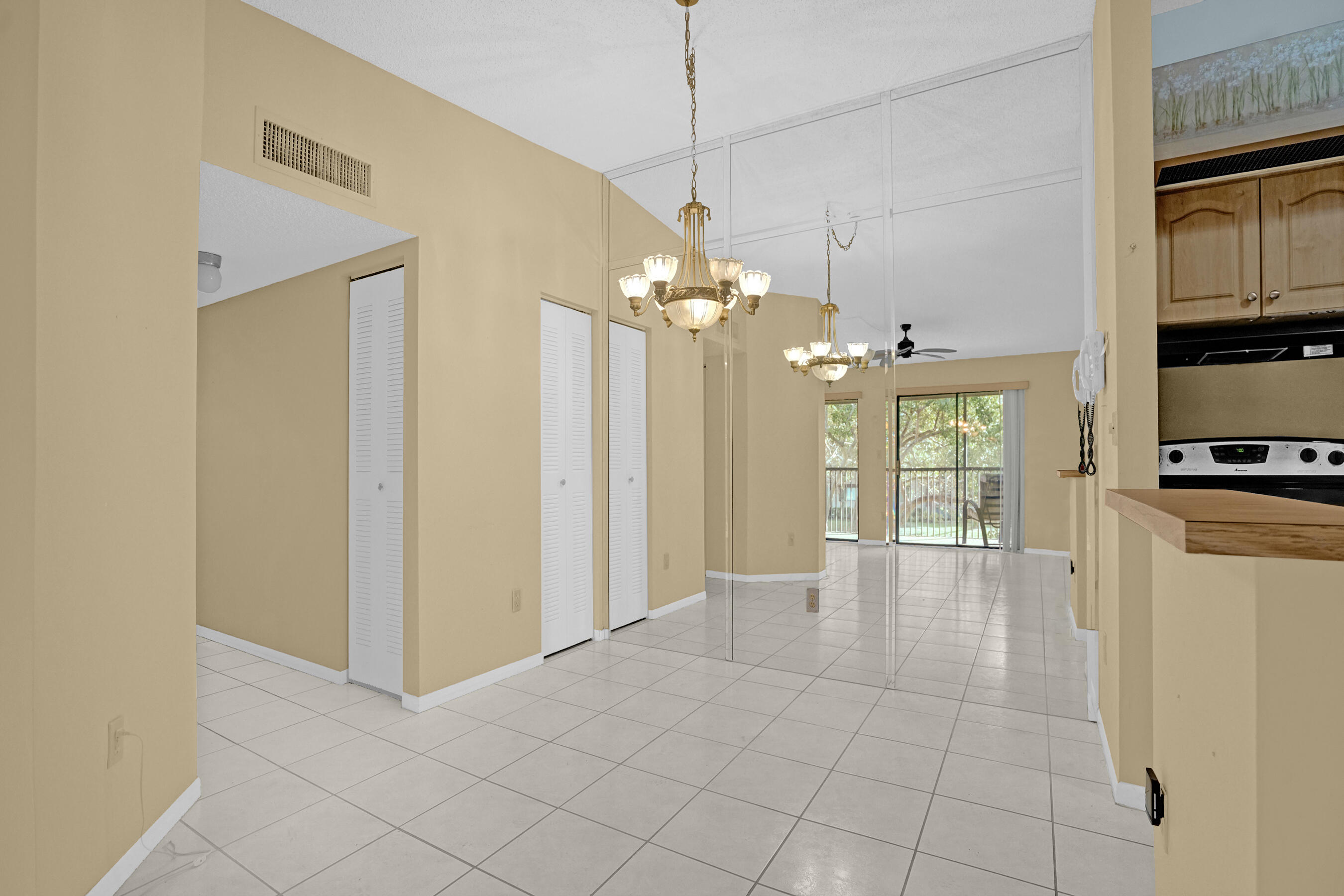 Empty living and dining area with mirrored wall, tiled floors, chandelier, and sliding doors to a balcony.
