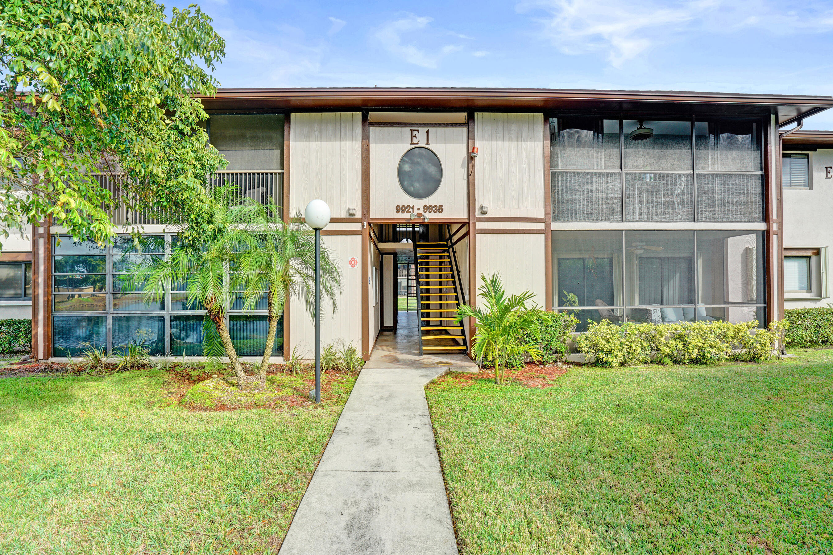 Condominium entrance with a central staircase, screened windows, and tropical landscaping.