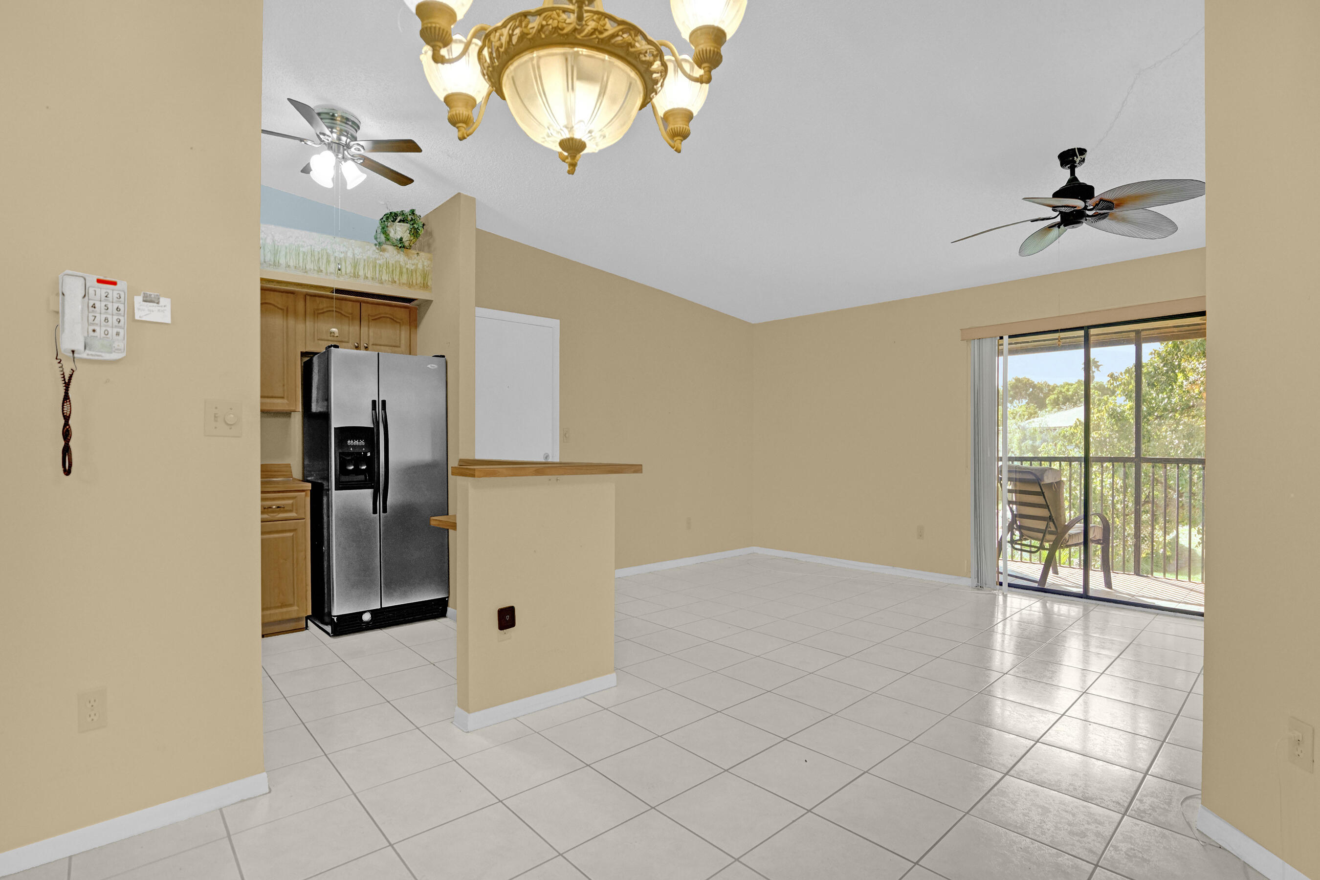 Open-plan kitchen and living area with tile floors, wood cabinets, and a sliding door to a leafy balcony.