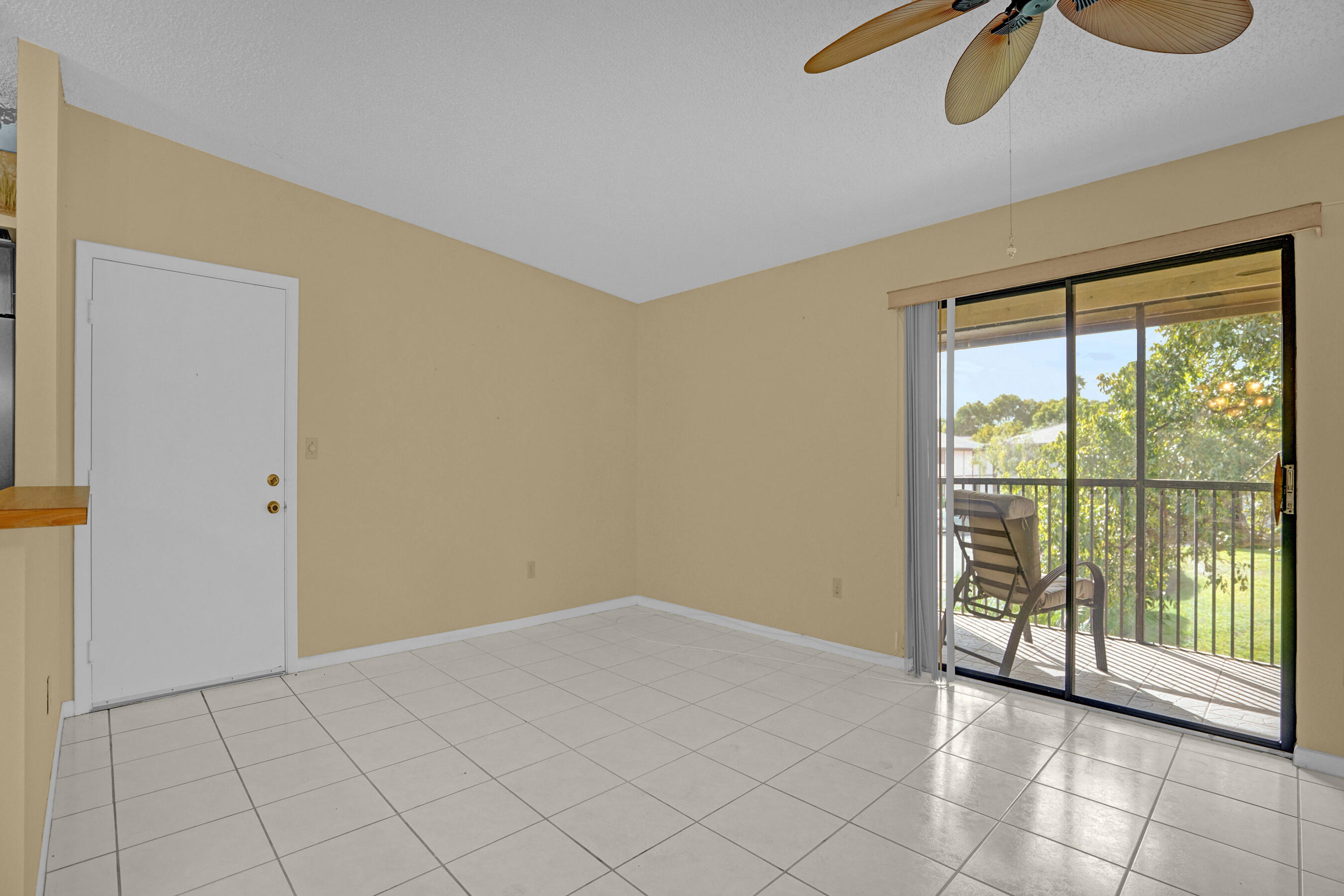 Empty tiled living room with beige walls and sliding doors to a balcony overlooking greenery.