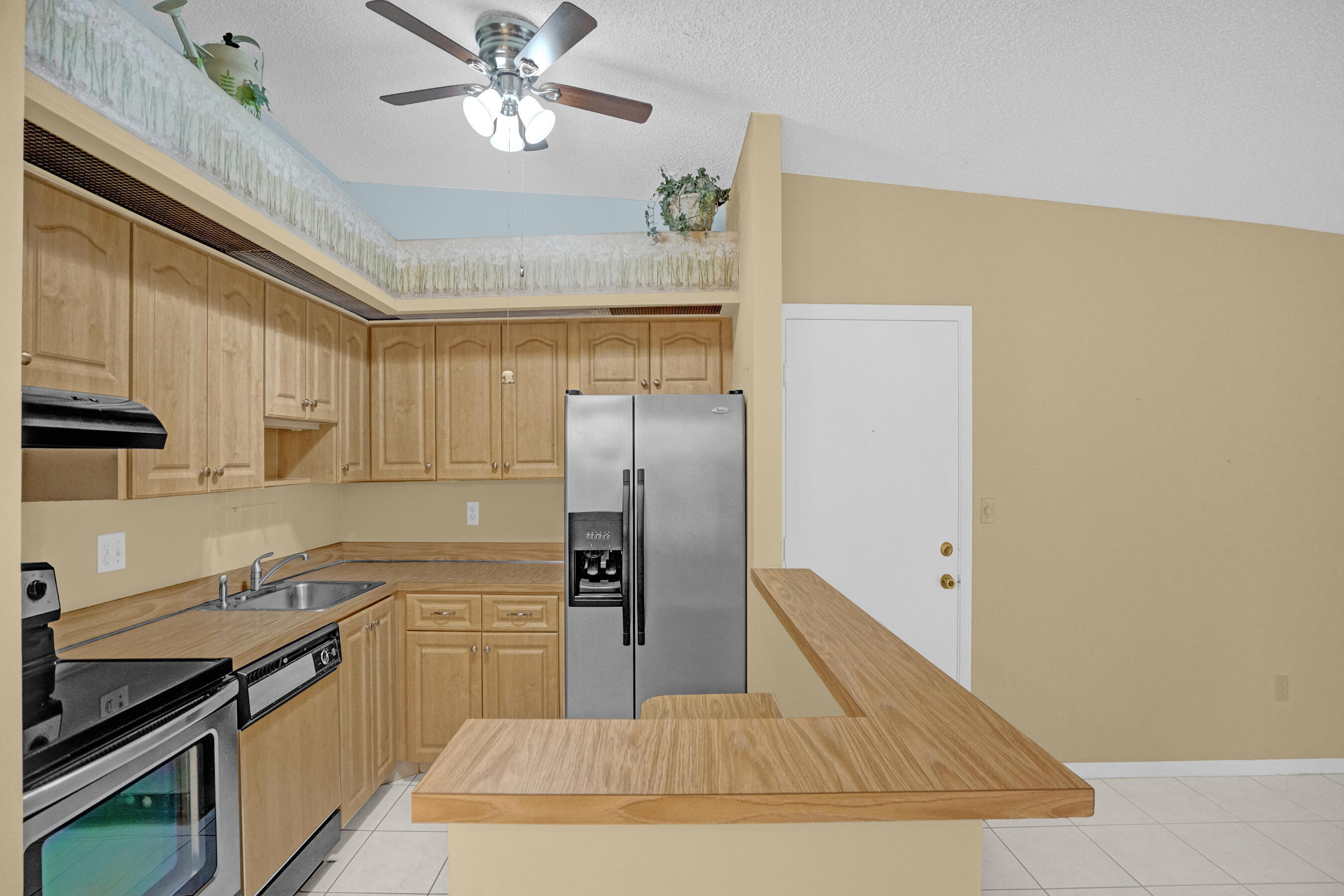 Kitchen with light wood cabinetry, stainless steel refrigerator, and a wood-topped breakfast bar.