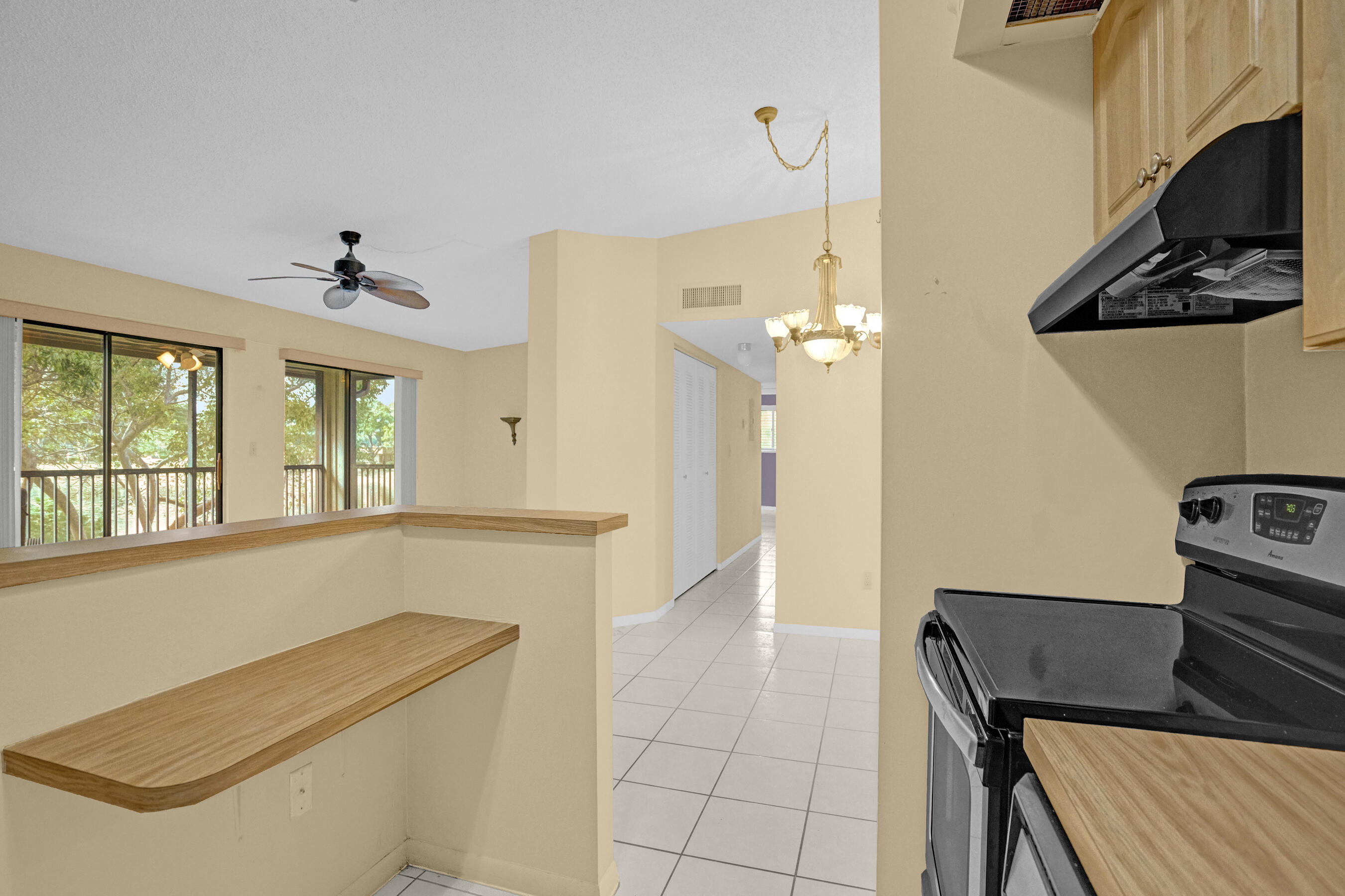 Kitchen with a black range, wood breakfast bar, tiled floor, and windows overlooking trees.