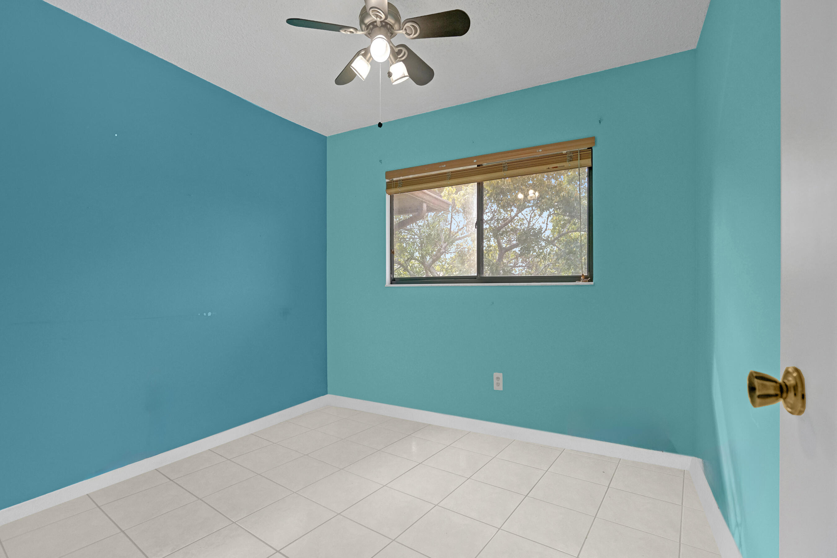 Empty turquoise room with white tile floors, a ceiling fan, and a window with wooden blinds.