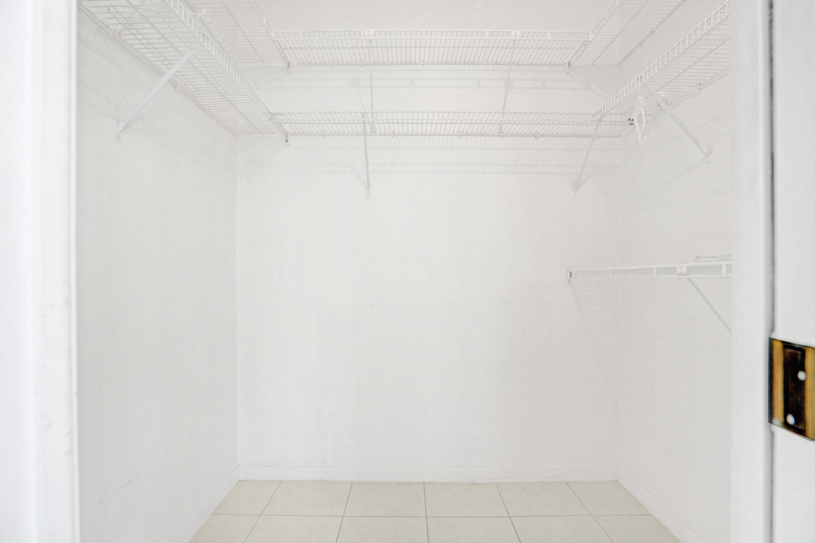 Empty walk-in closet with extensive white wire shelving and a light tiled floor.