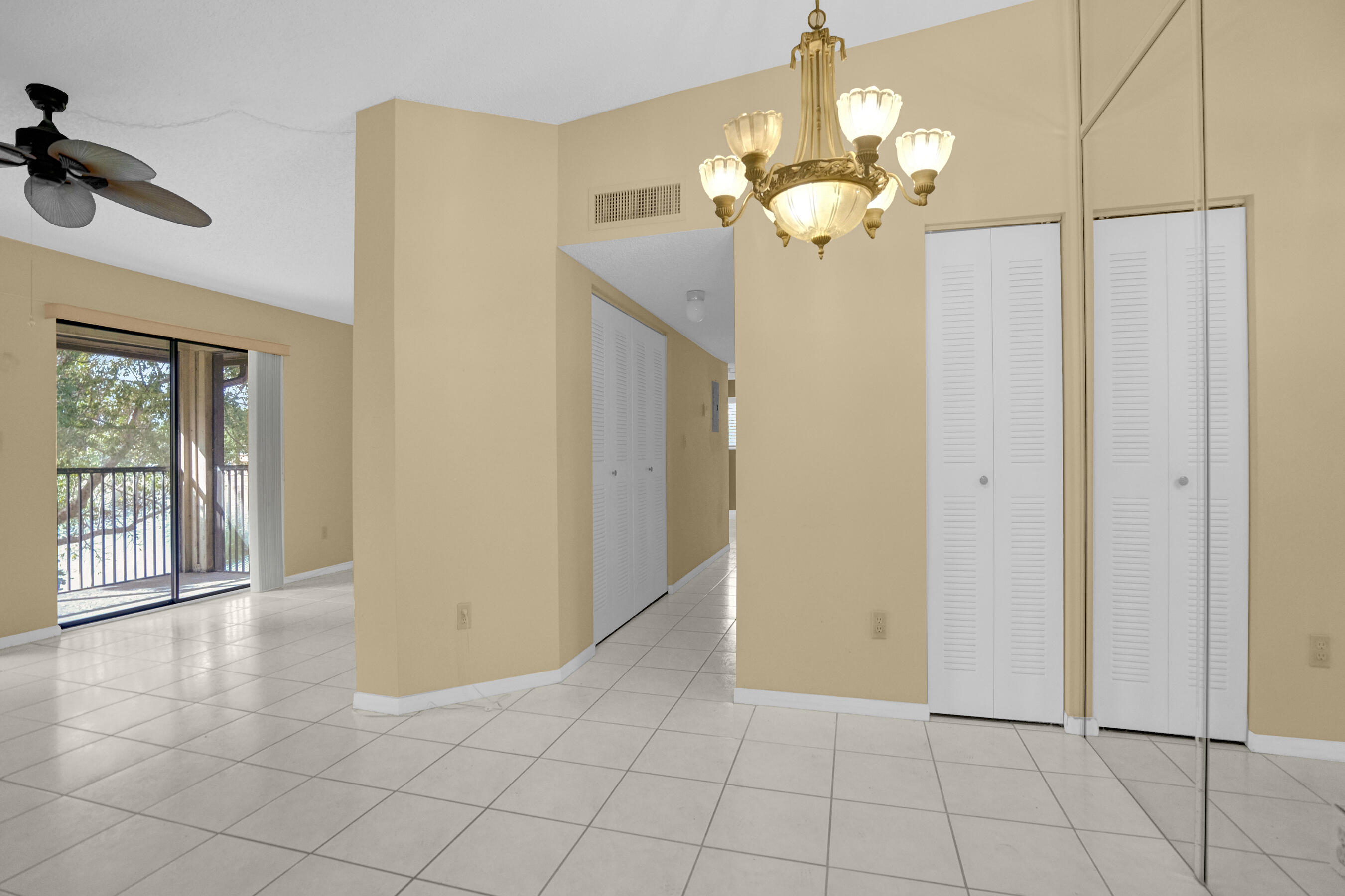 Vacant apartment interior with tiled floors, mirrored closet doors, a chandelier, and sliding glass doors to a balcony.