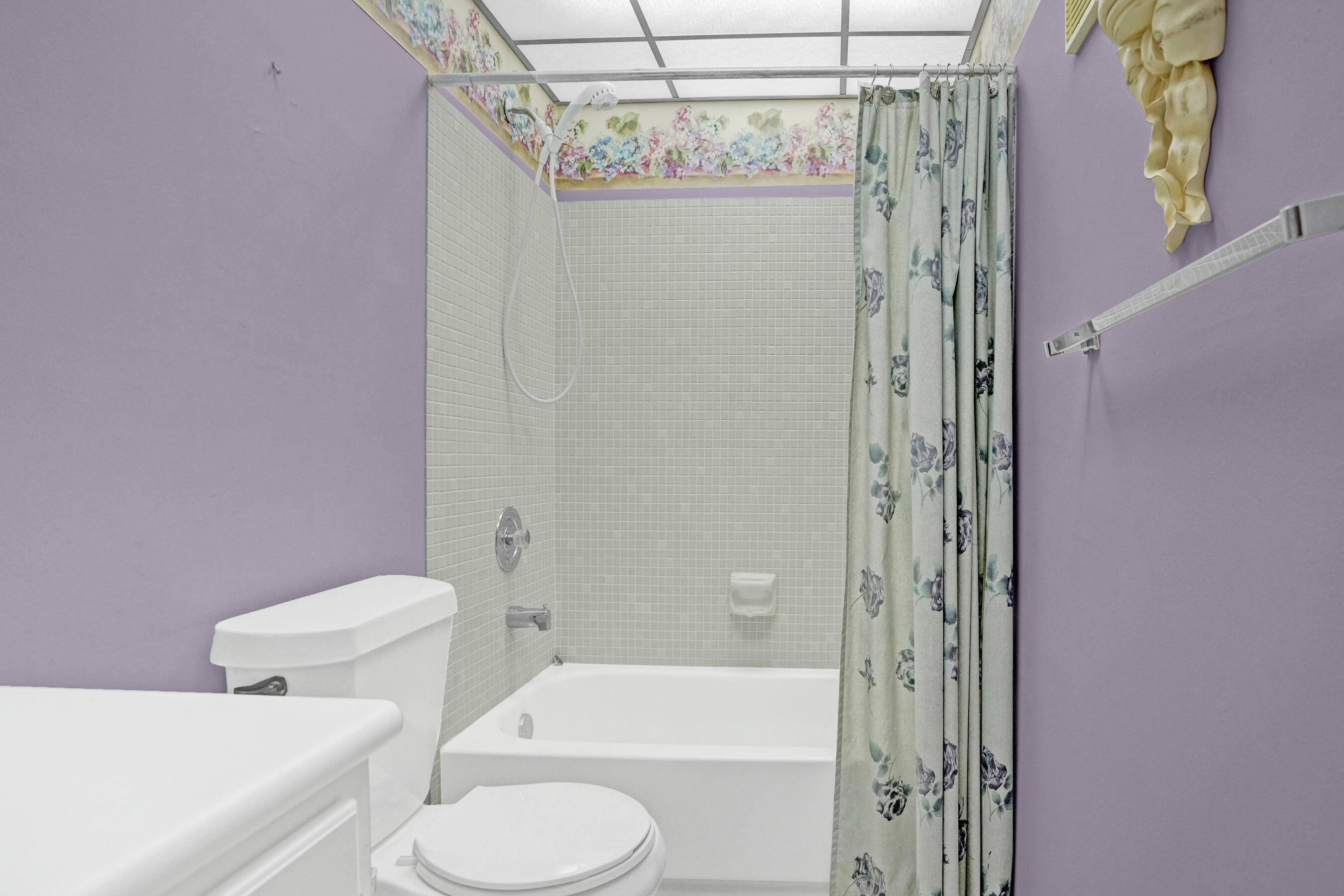 Bathroom with a tiled tub and shower, floral curtain, and lavender walls.