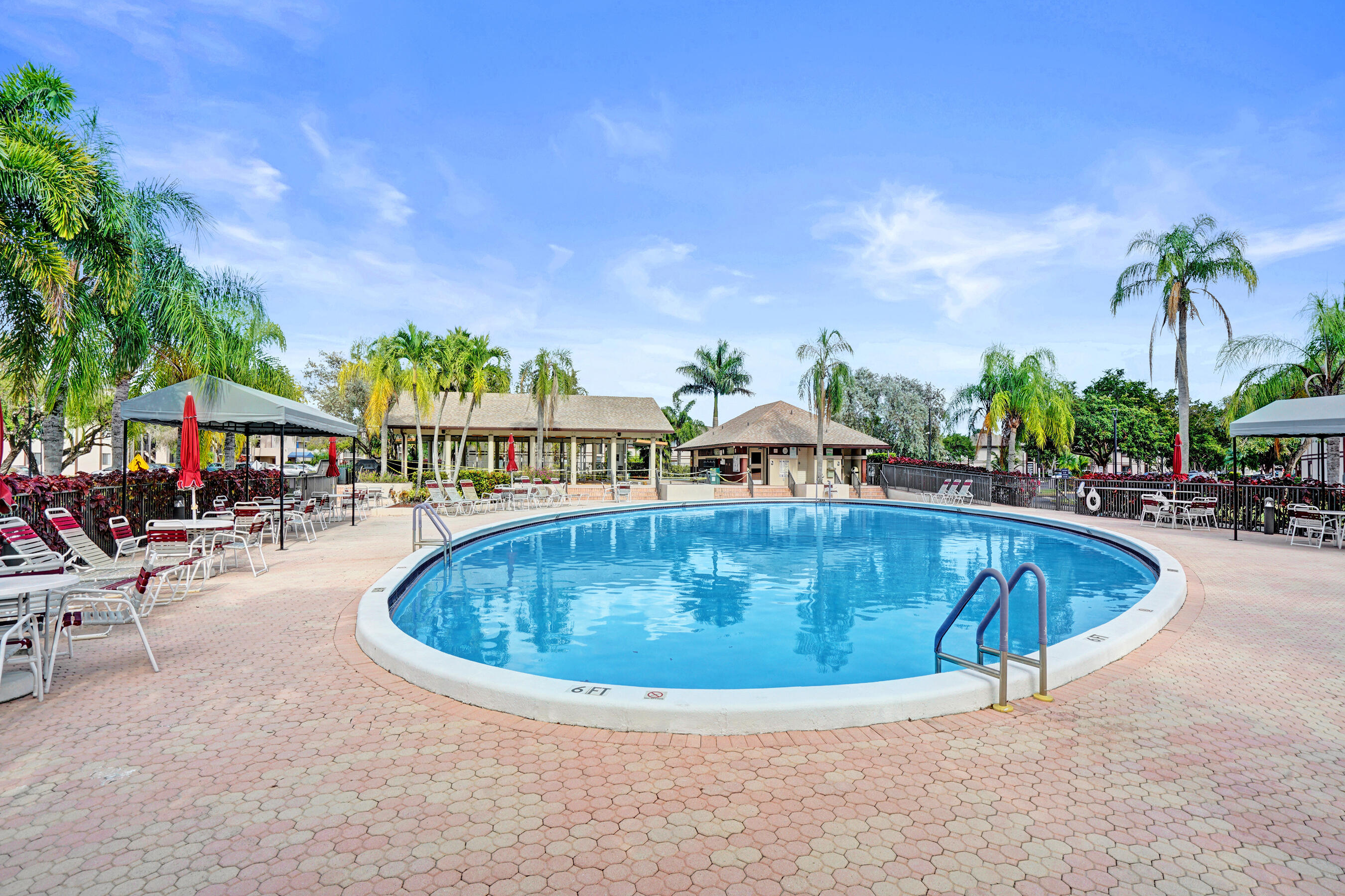 Community swimming pool surrounded by lounge chairs, shaded canopies, and palm trees.