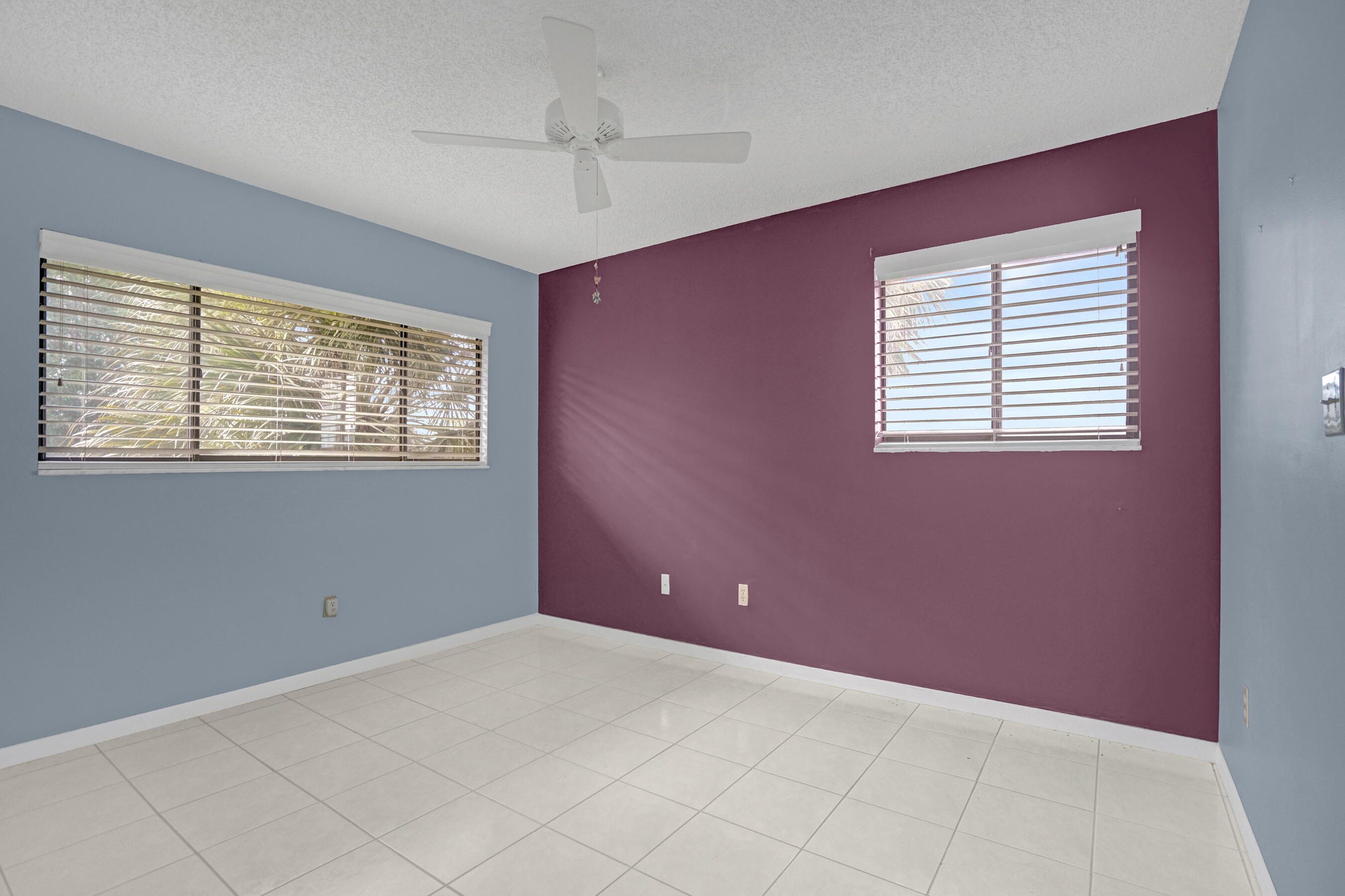 Vacant room with tiled floors, a ceiling fan, and two windows with blinds.
