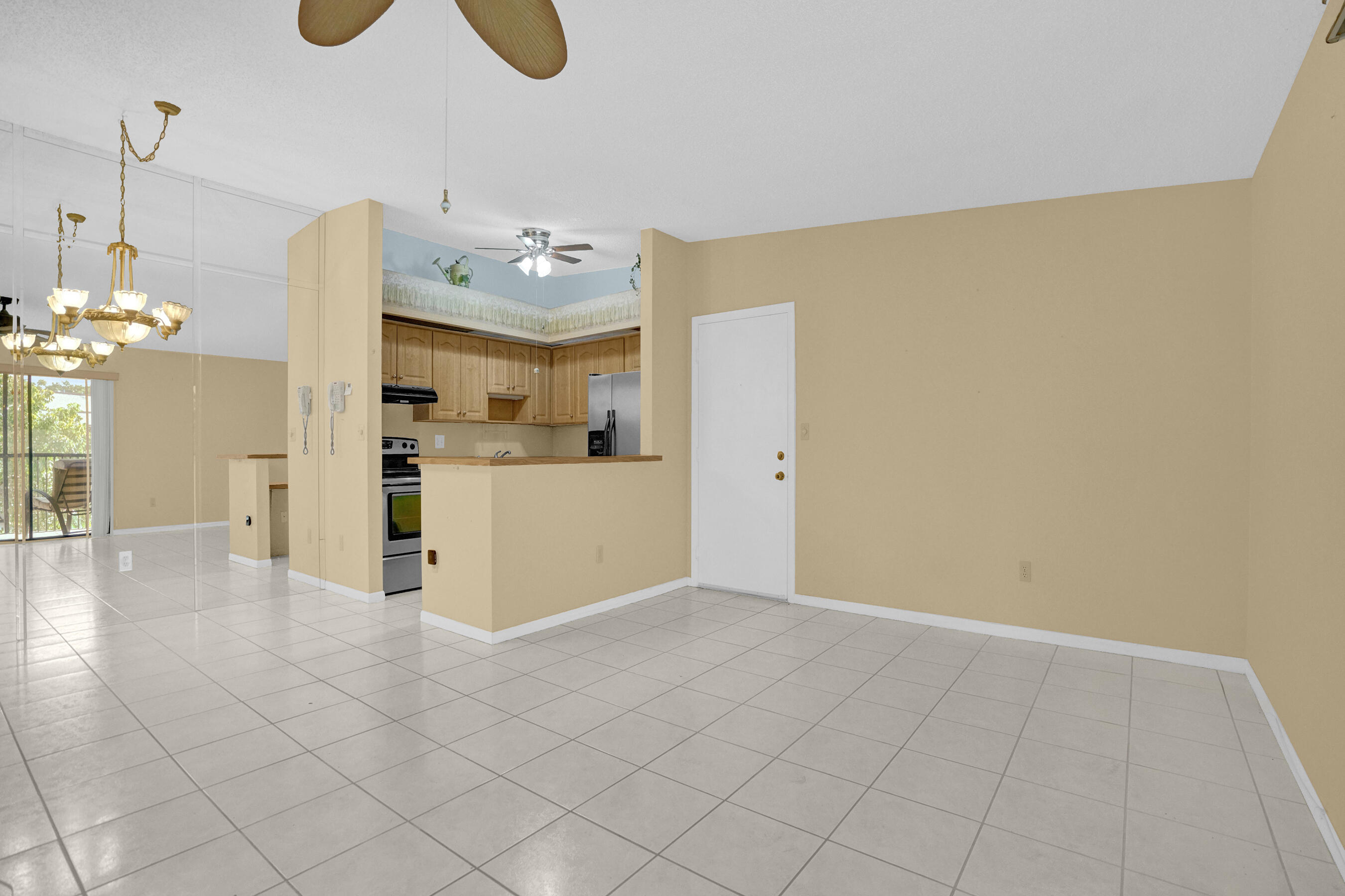 Vacant tiled living area with mirrored walls, a chandelier, and an open kitchen with wood cabinets.