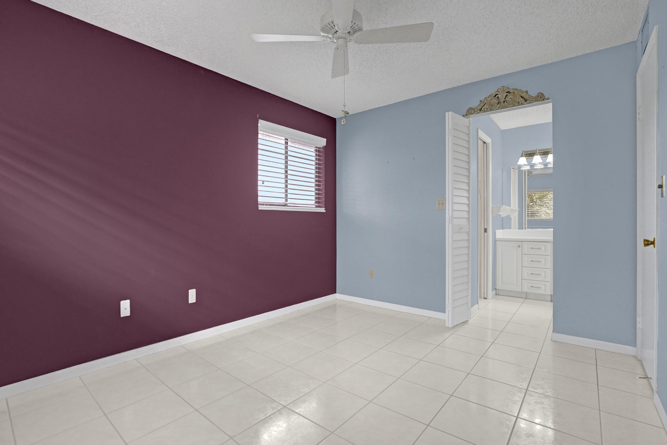 Empty bedroom with burgundy and blue walls, tiled floor, and an open doorway to a bathroom.