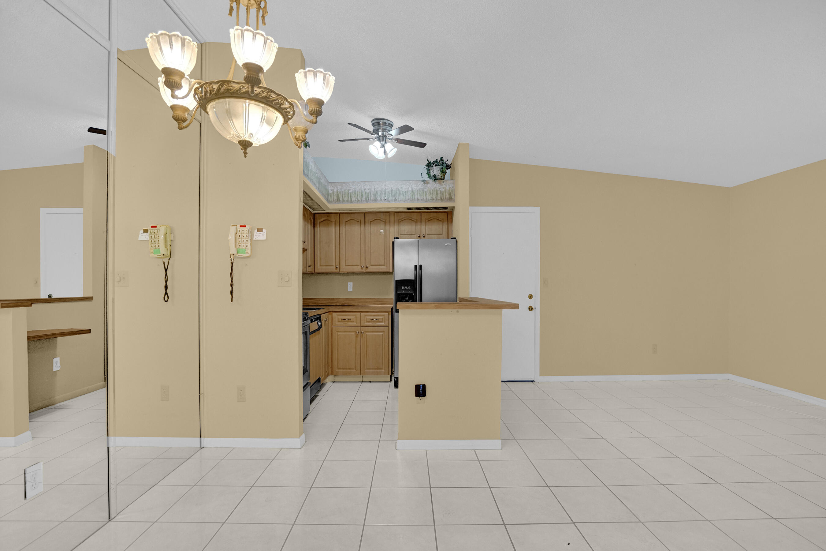 Unfurnished condo living area with tiled floors, mirrored wall, chandelier, and open kitchen.