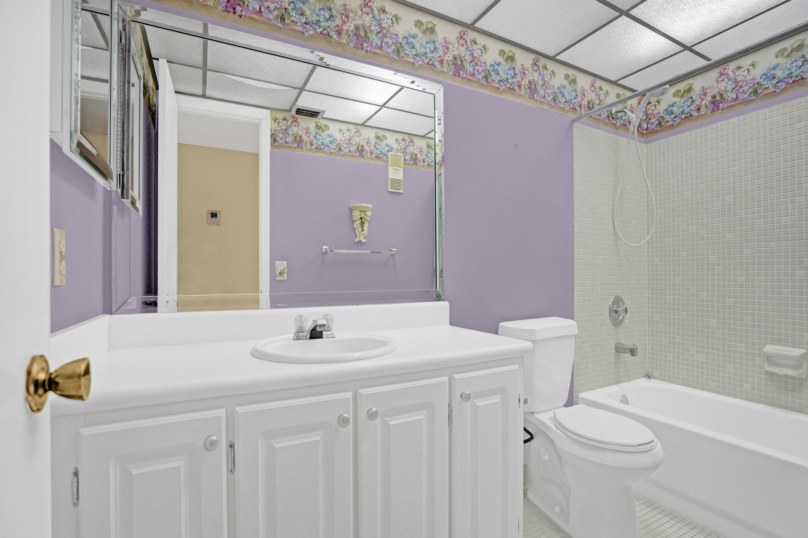 Bathroom with a white vanity, toilet, and tiled bathtub against lavender walls with a floral border.