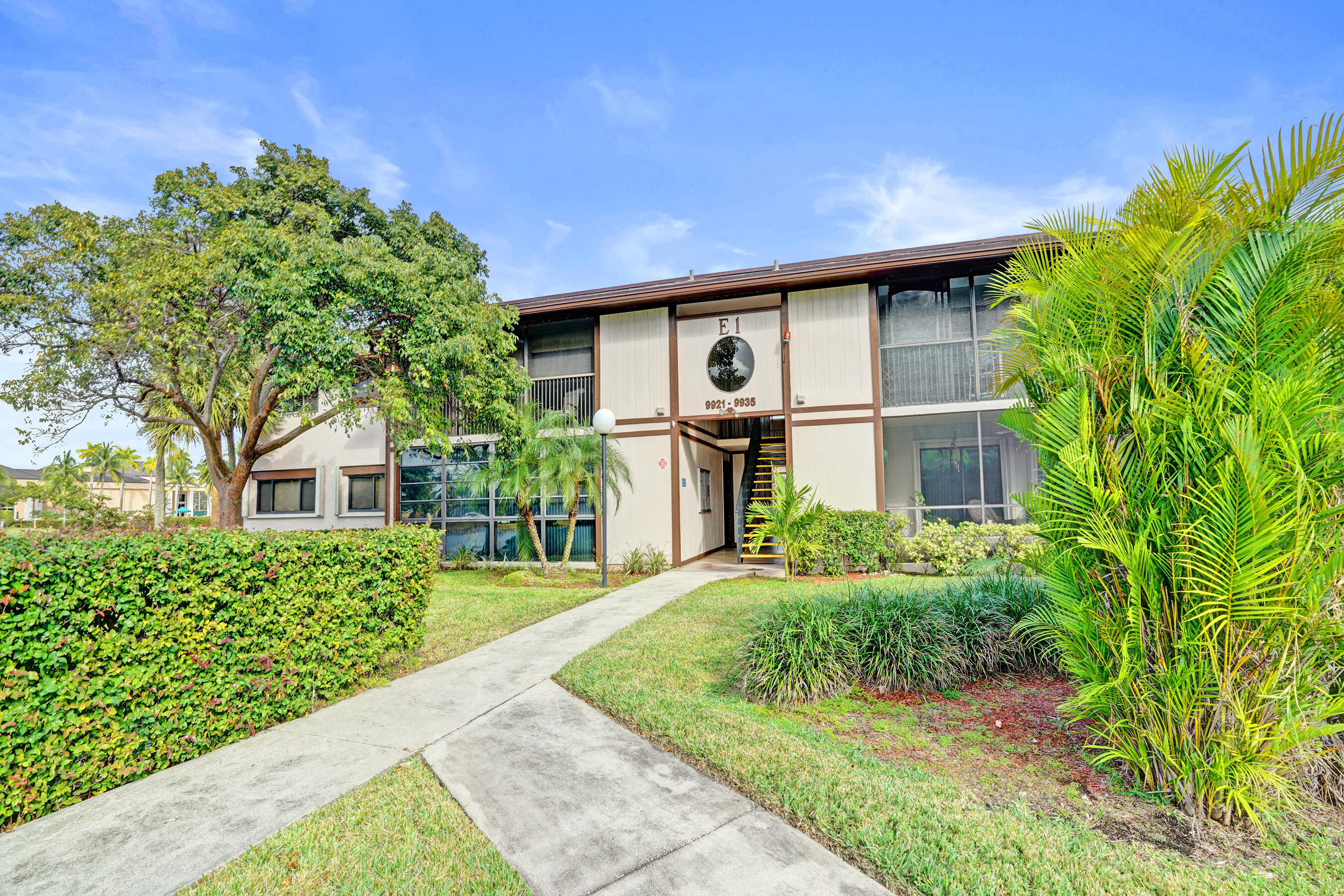 Two-story residential building entrance framed by palm trees and a landscaped walkway.