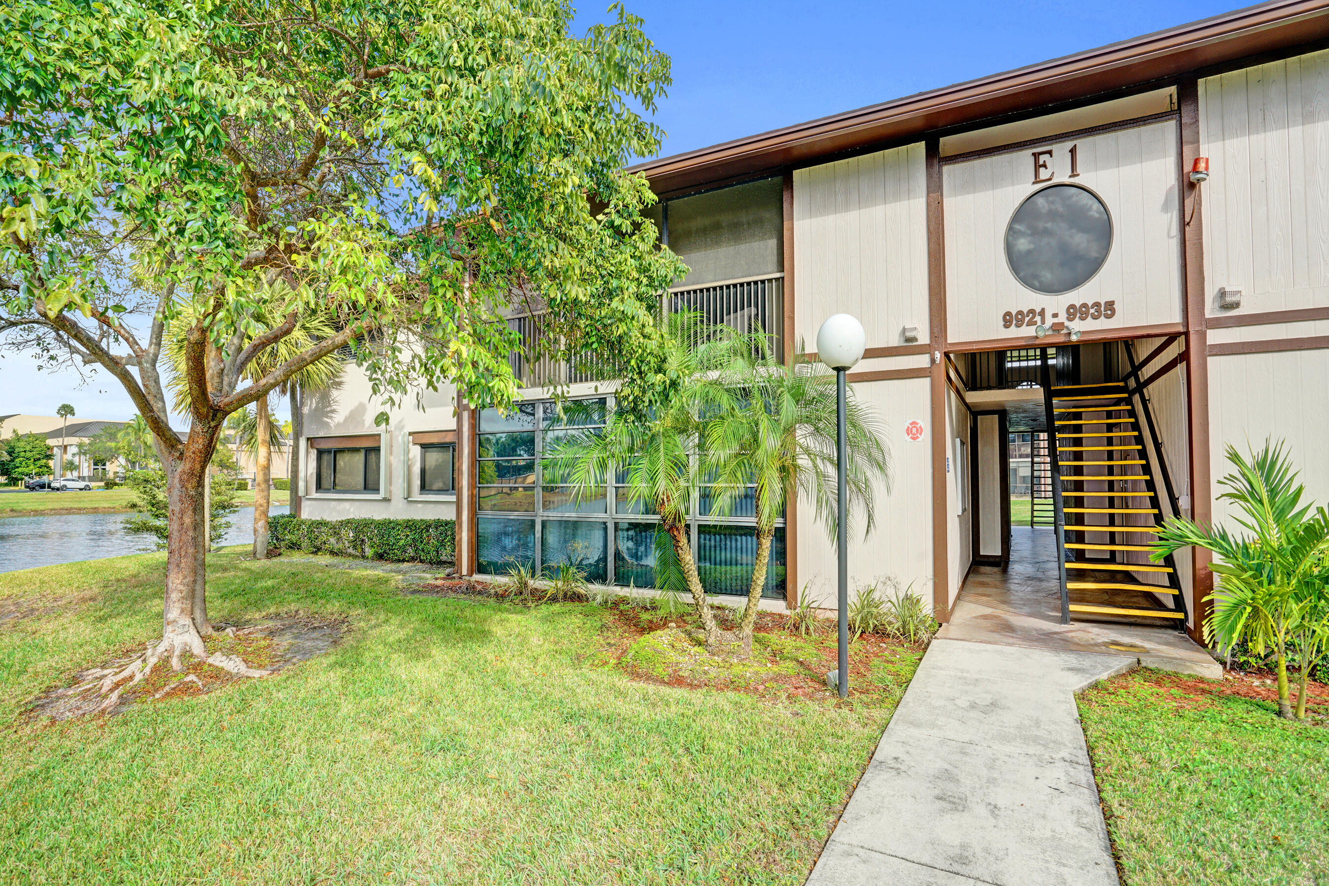 Condominium entrance with an exterior stairwell, landscaped lawn, and canal beside the building.