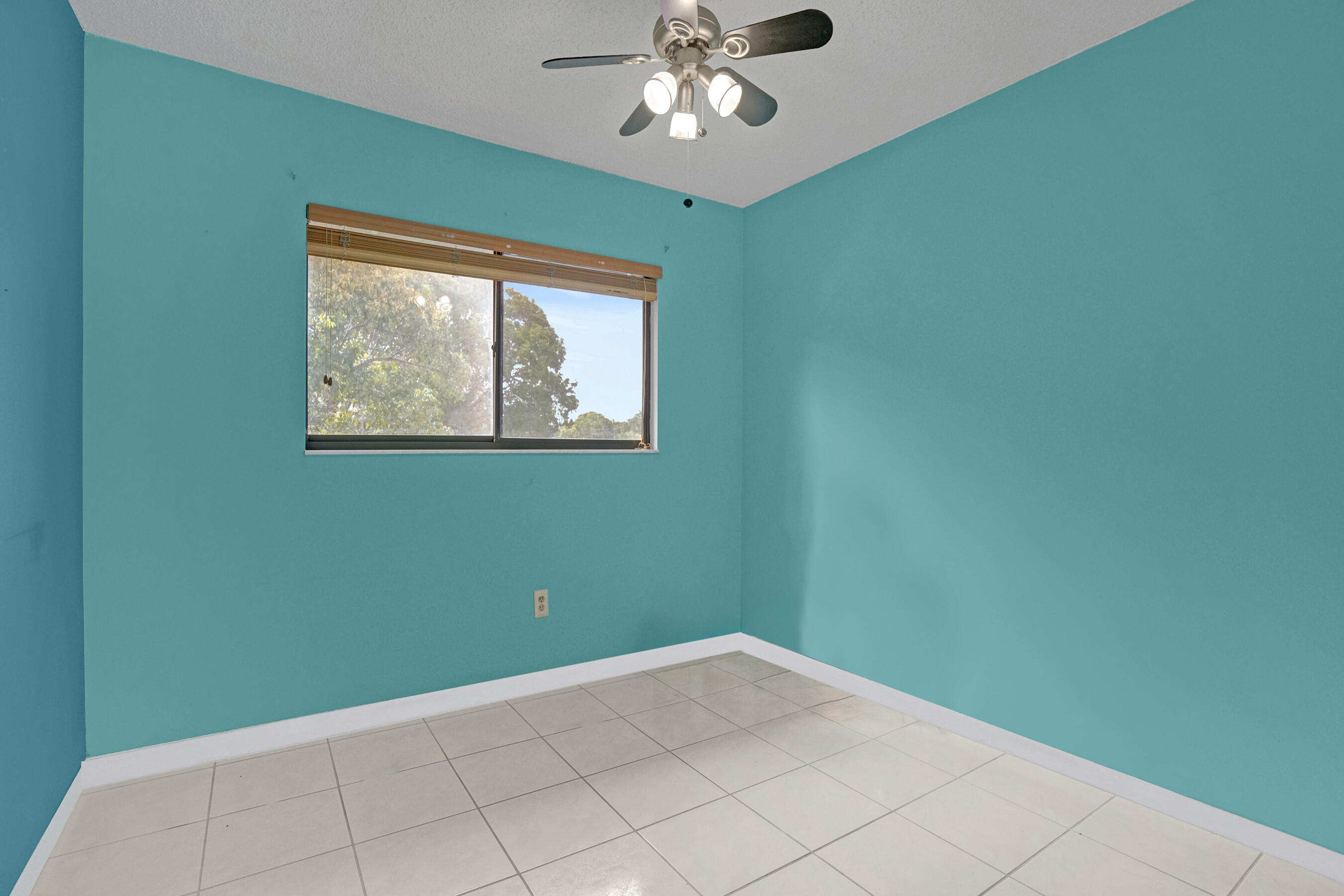 Empty turquoise room with a tiled floor, window with wooden blinds, and ceiling fan.