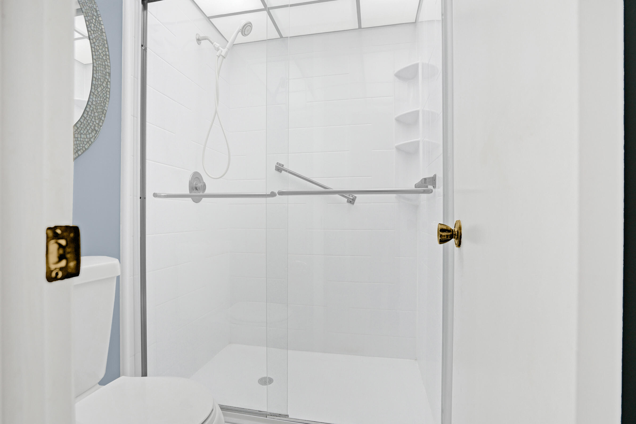 Bathroom with a white-tiled glass shower, chrome grab bars, and built-in corner shelves.