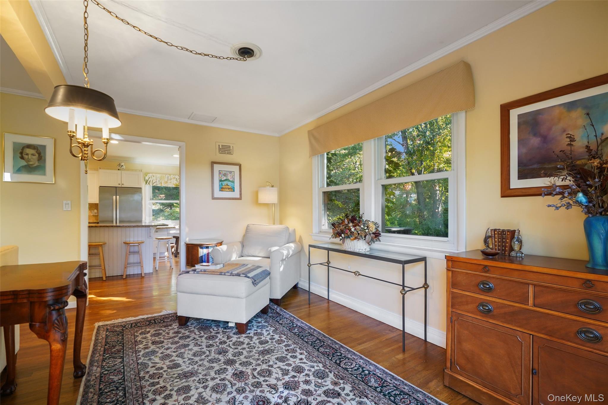 Living room with a white chaise lounge, patterned rug, hardwood floors, and large windows overlooking trees.