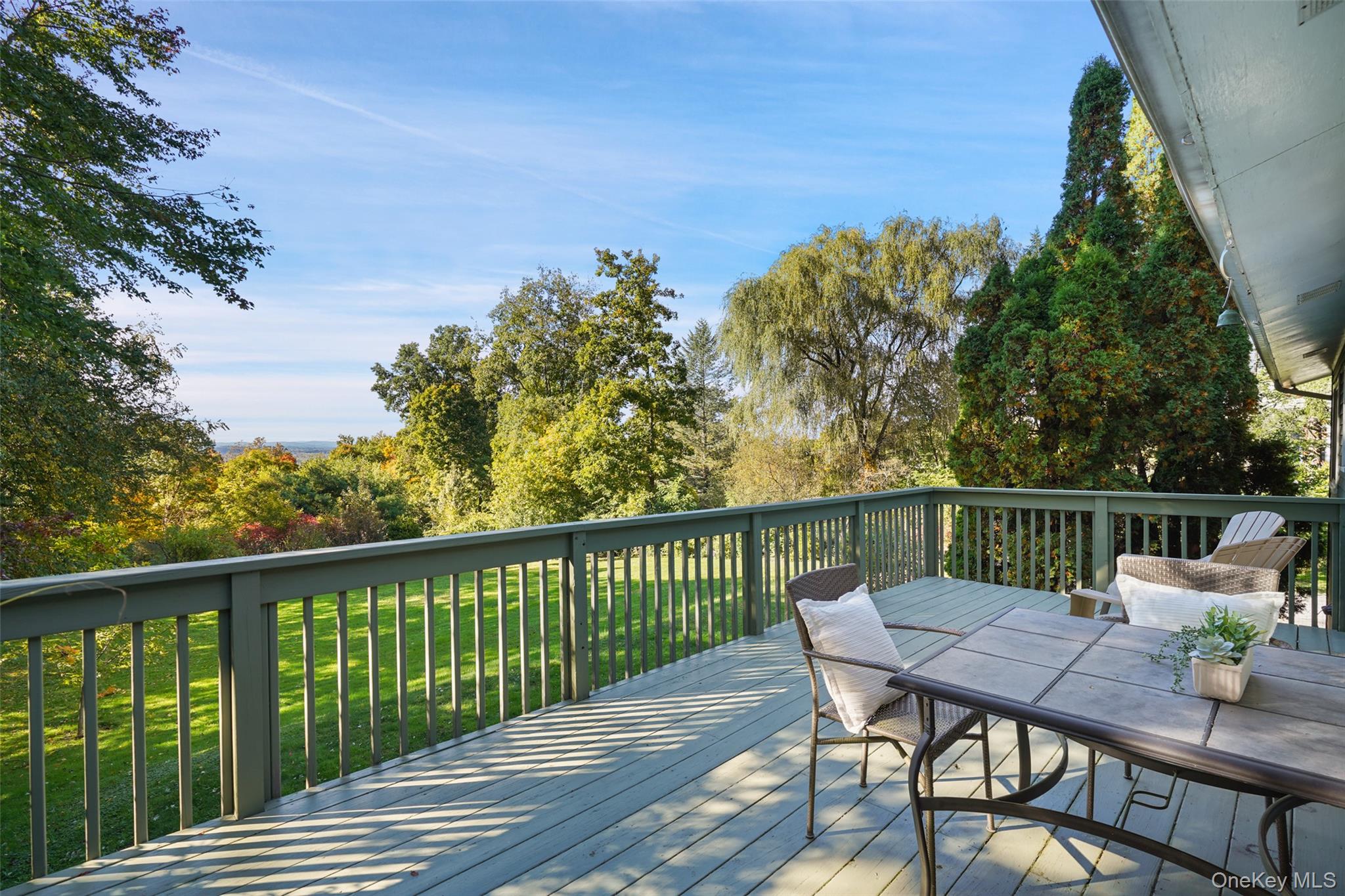 Wooden deck with outdoor dining set overlooking a lawn, autumn trees, and distant wooded hills.
