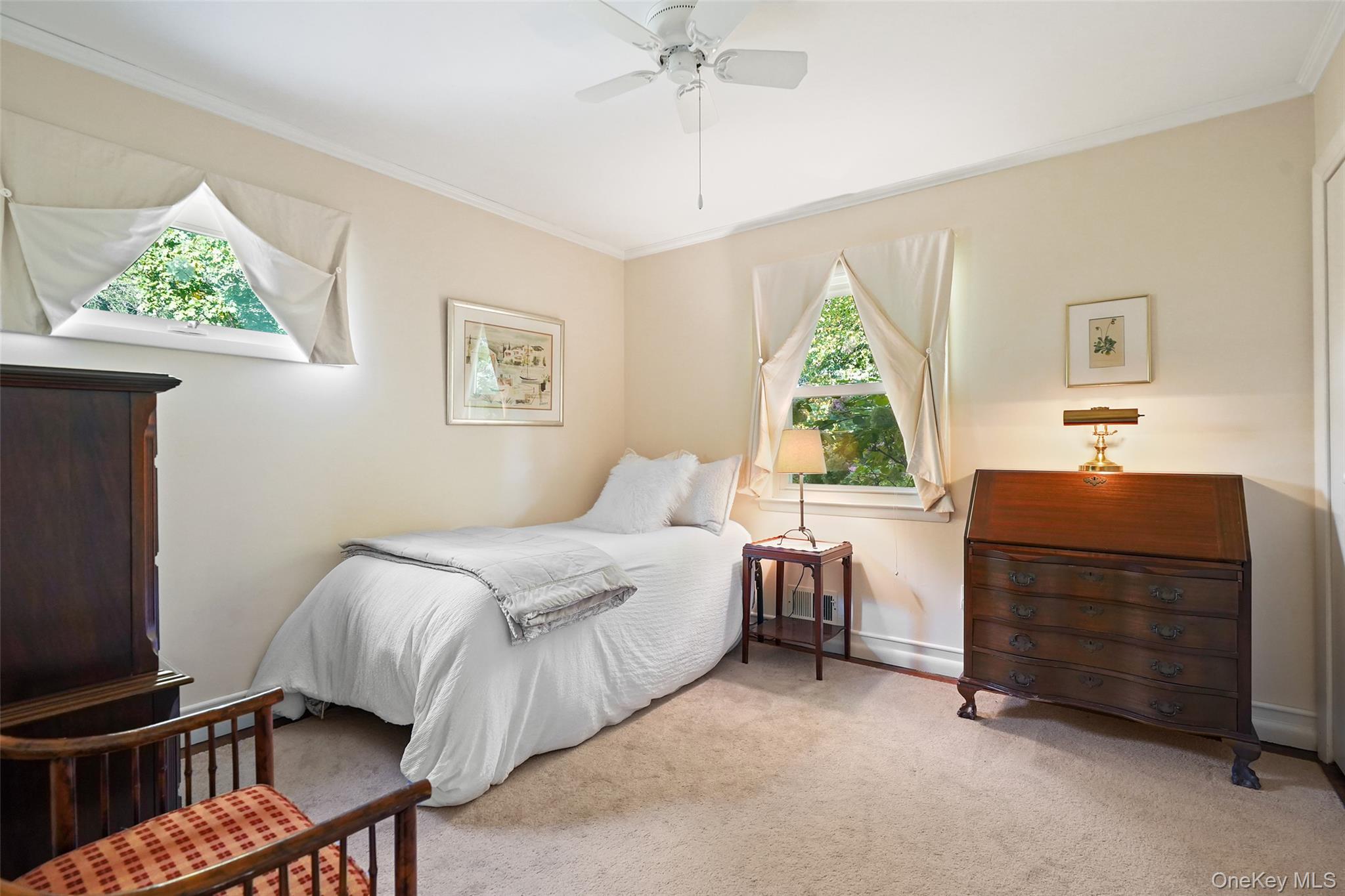Bedroom with a white bed, curtained windows, and dark wooden furniture.