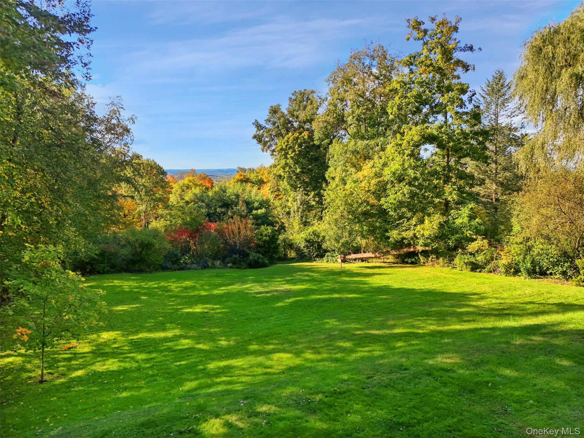 Expansive green lawn bordered by autumn trees, with distant hills visible beyond the property.