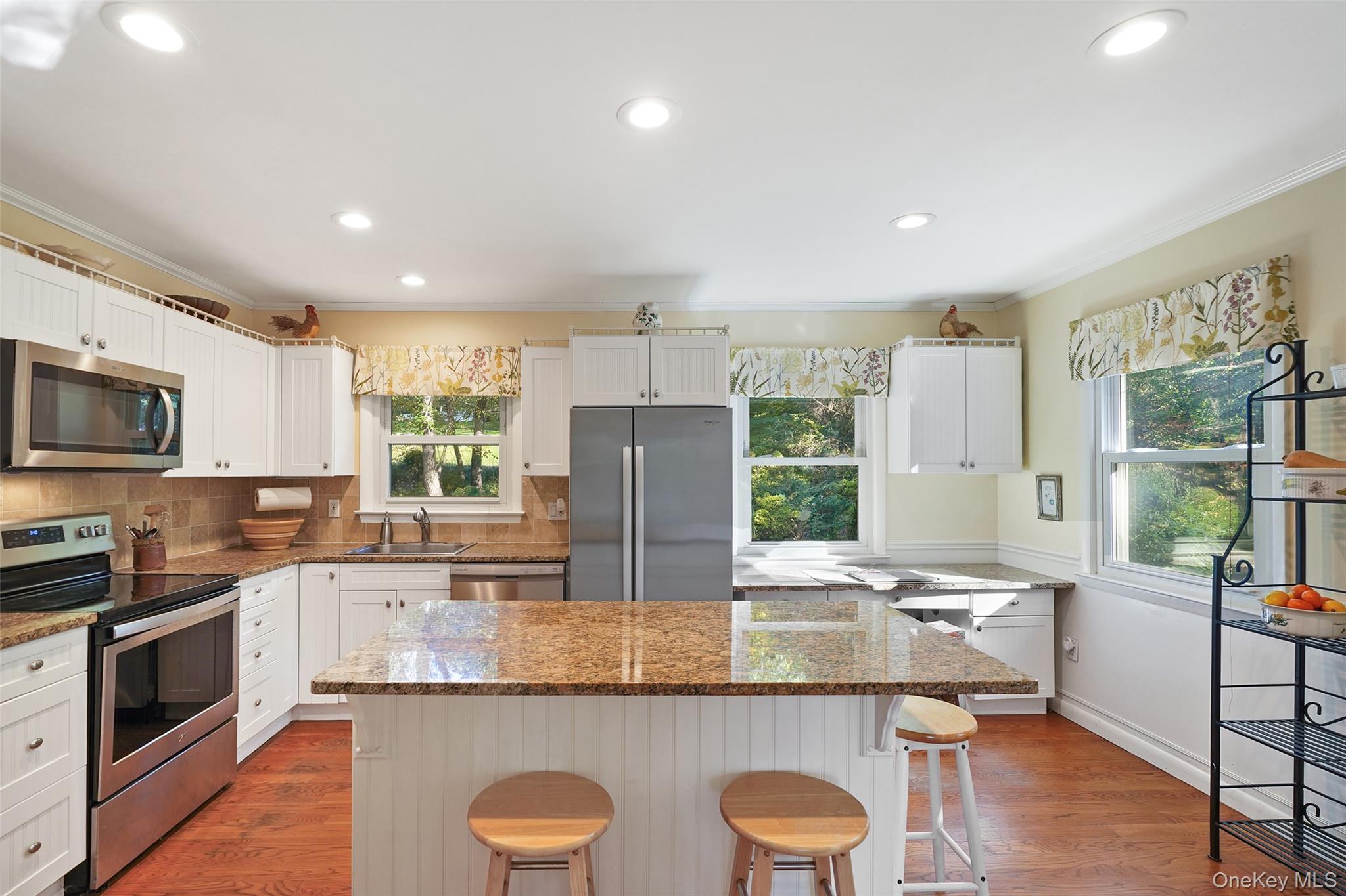 Bright kitchen with white cabinets, stainless steel appliances, and a granite island with two stools.