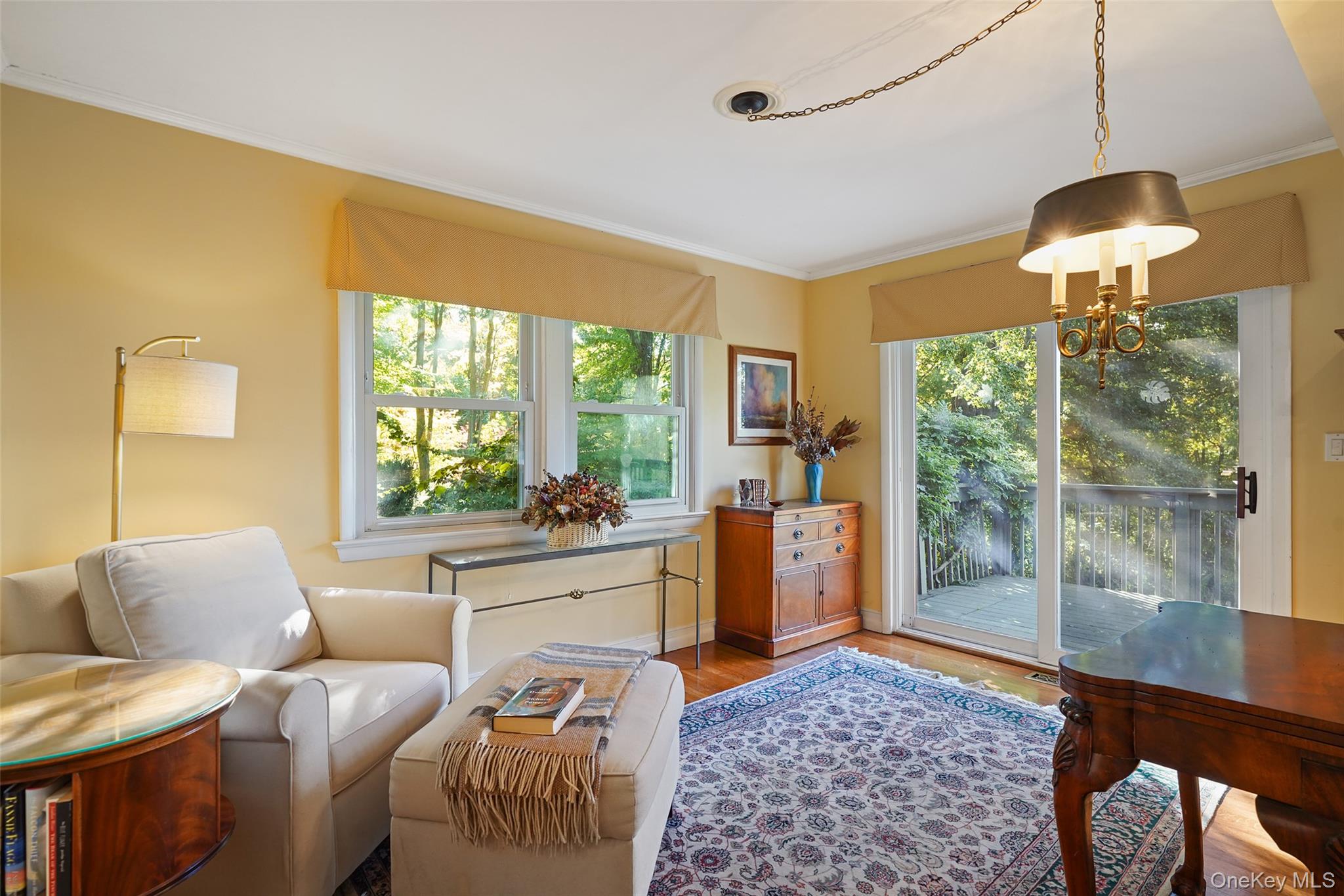 Furnished living room with white seating, patterned rug, and sliding doors to a wooded deck.