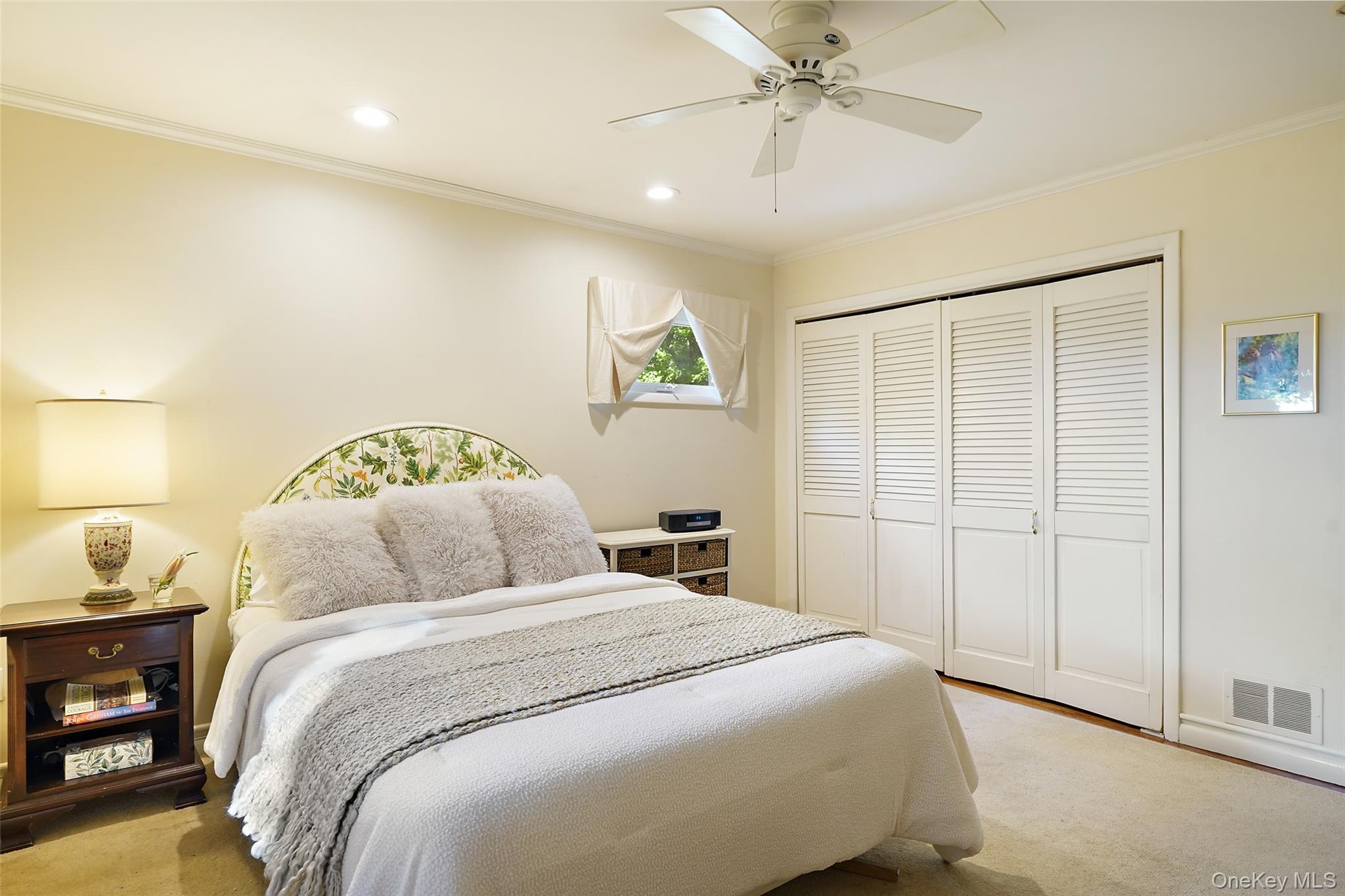 Furnished bedroom with a white bed, floral headboard, and louvered closet doors.