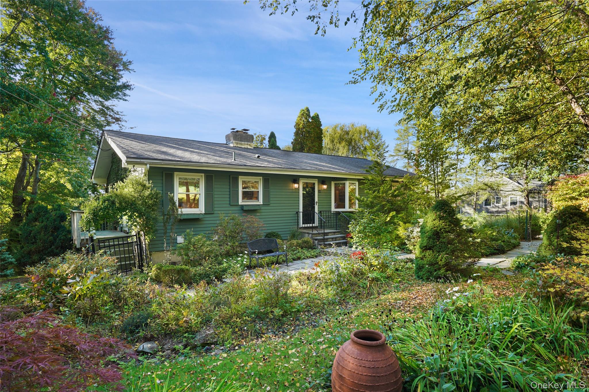 Green single-story home framed by mature trees, with a garden path and front steps.