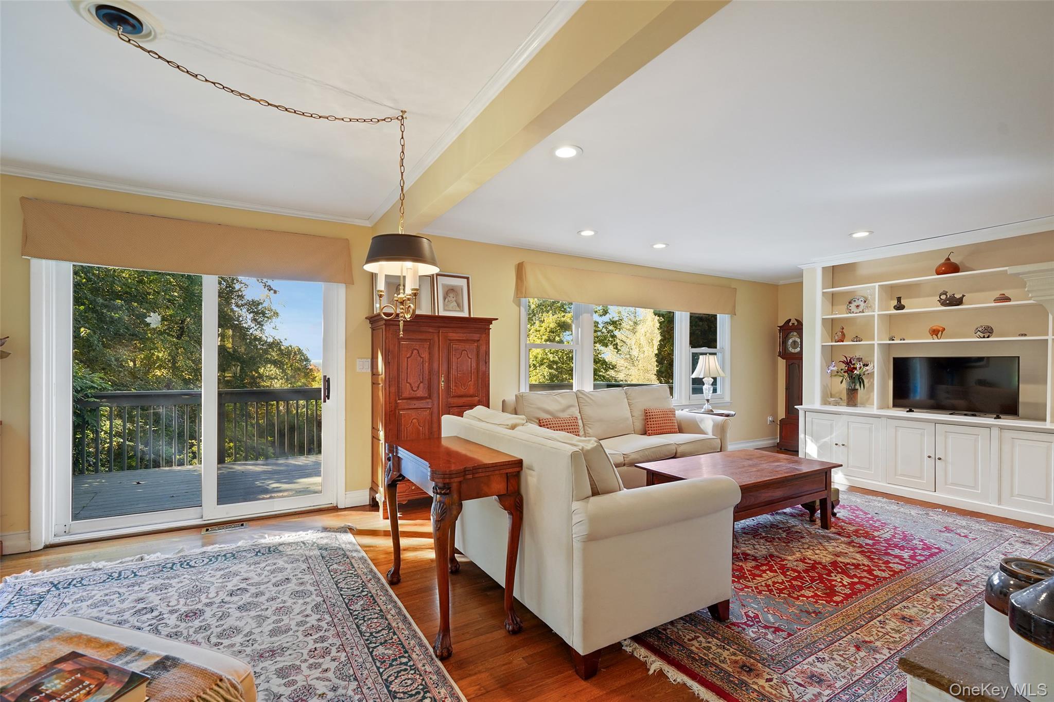 Living room with cream sofas, patterned rugs, built-in shelving, and sliding doors to a tree-lined deck.