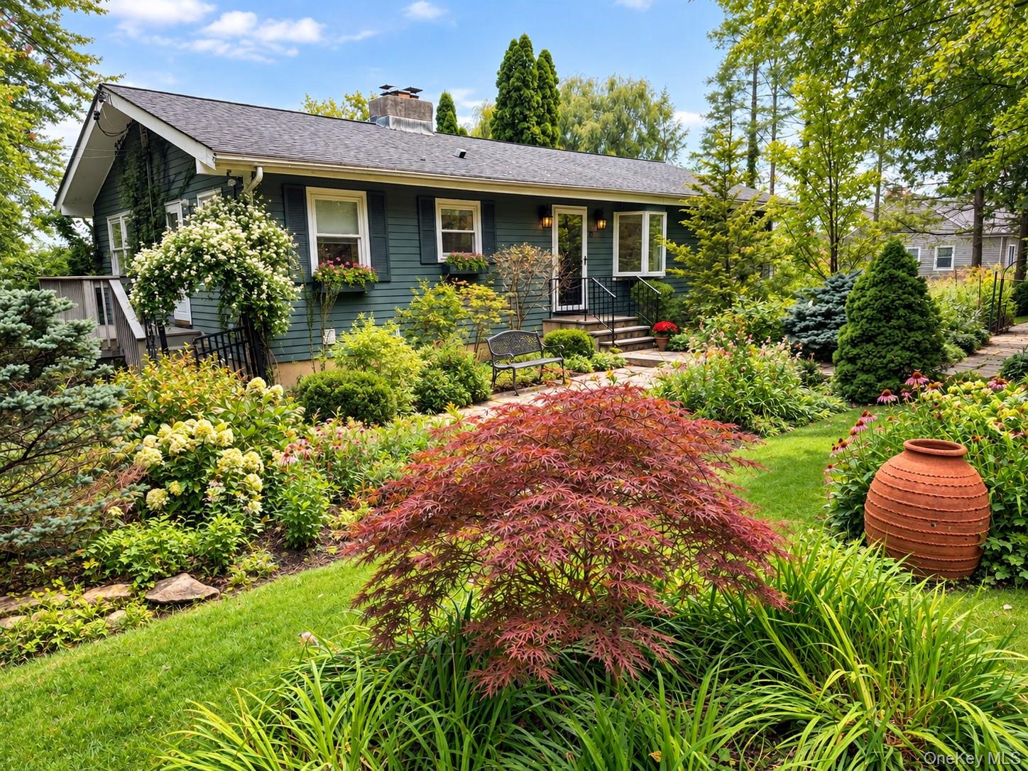Dark green single-story home with a gray roof, framed by lush flowering gardens.