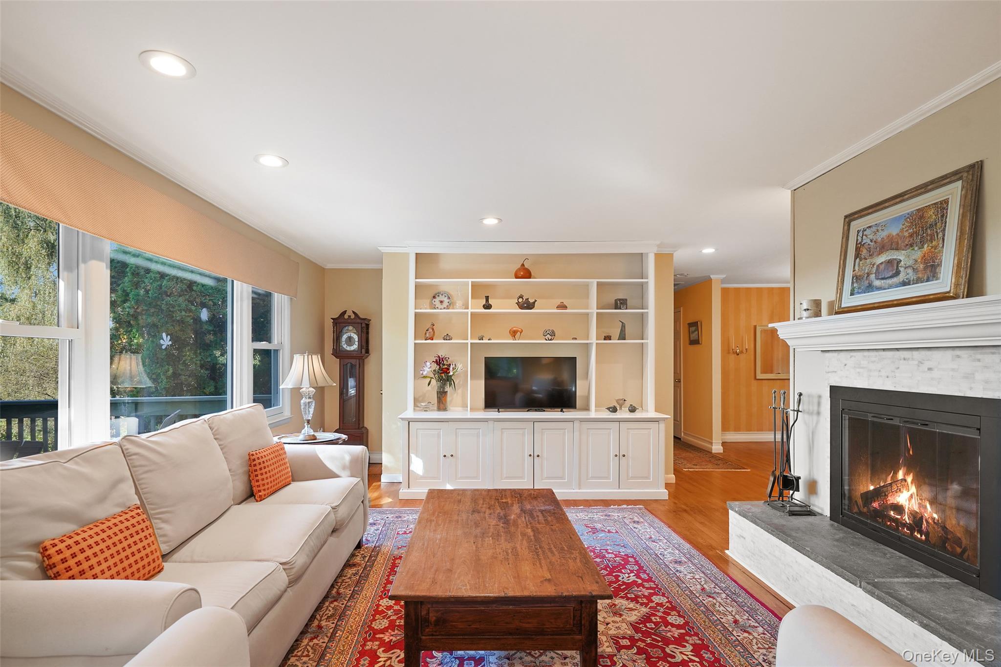 Living room with built-in shelving, a cream sectional, and a lit fireplace beside large windows.