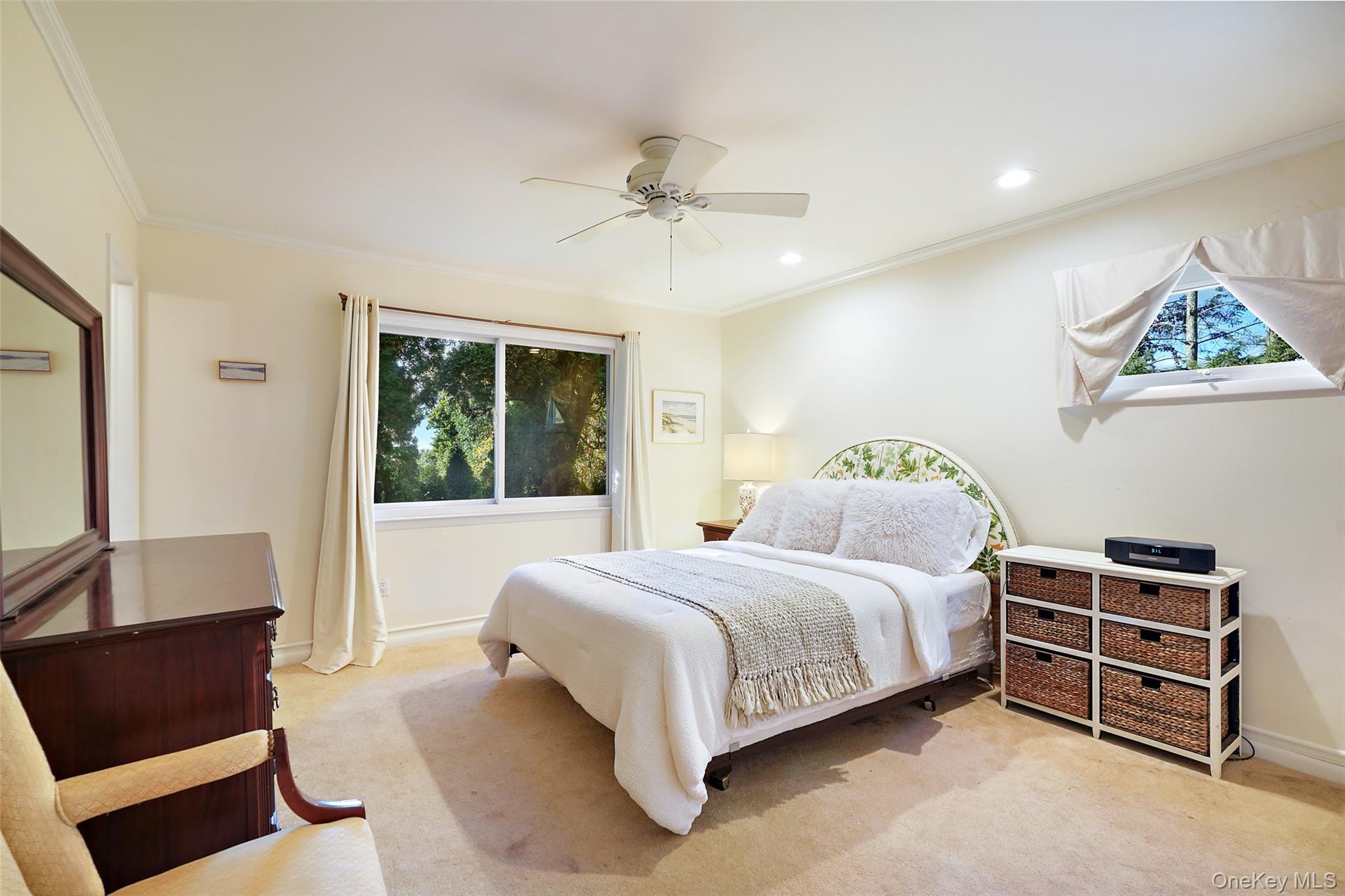 Furnished bedroom with a white bed, floral headboard, ceiling fan, and large window.