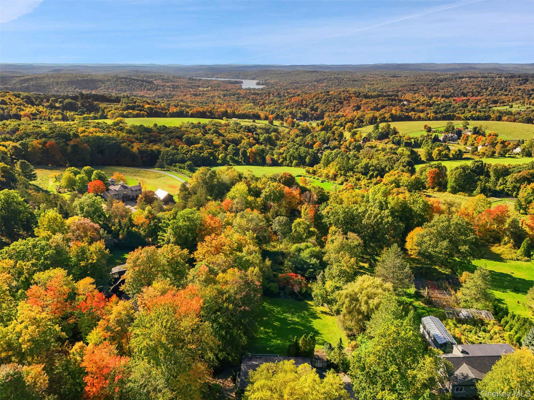 Aerial view of a wooded estate with broad lawns and a greenhouse amid autumn foliage.