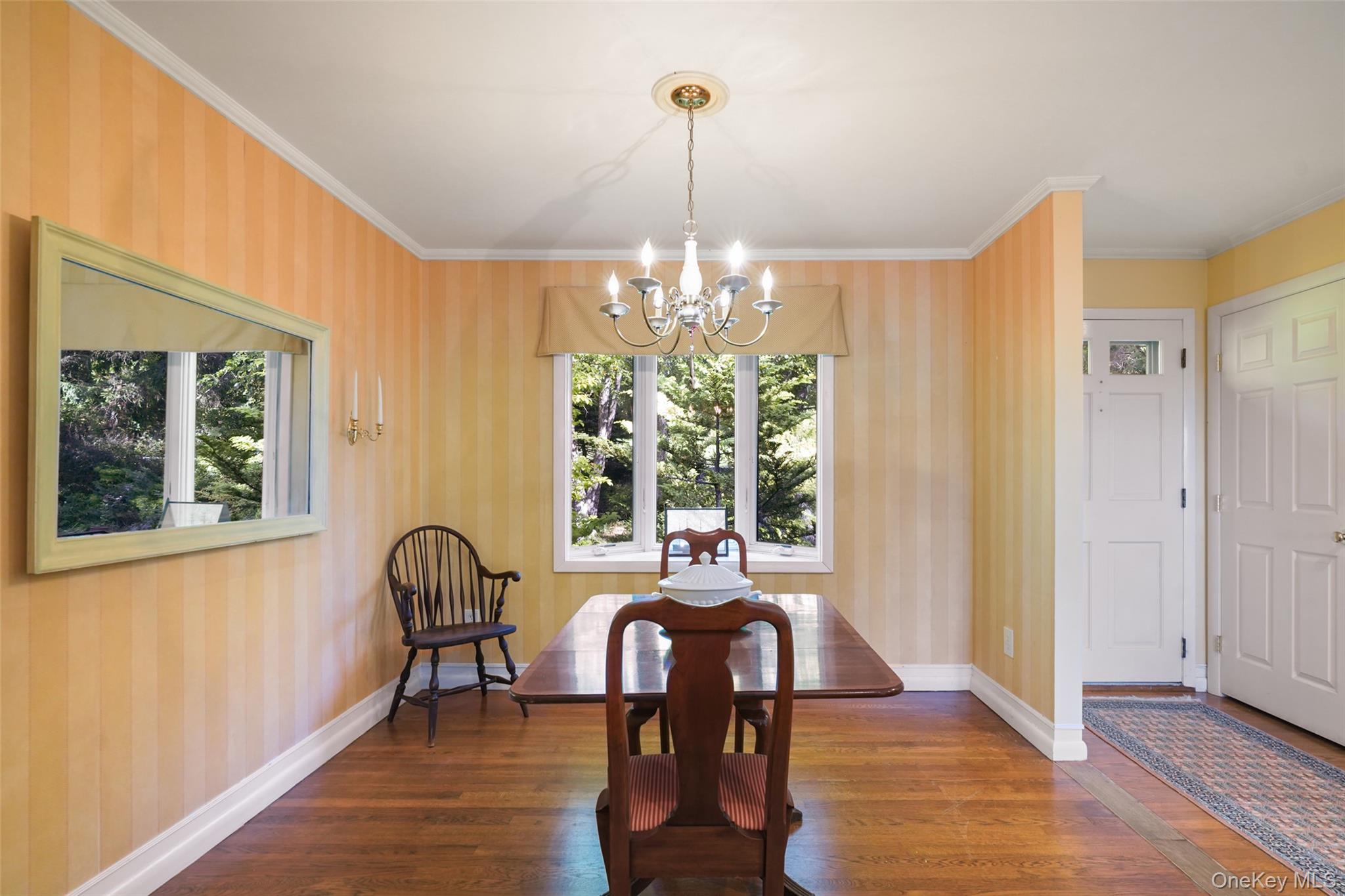 Dining room with a wooden table, chandelier, striped yellow walls, and hardwood floors.