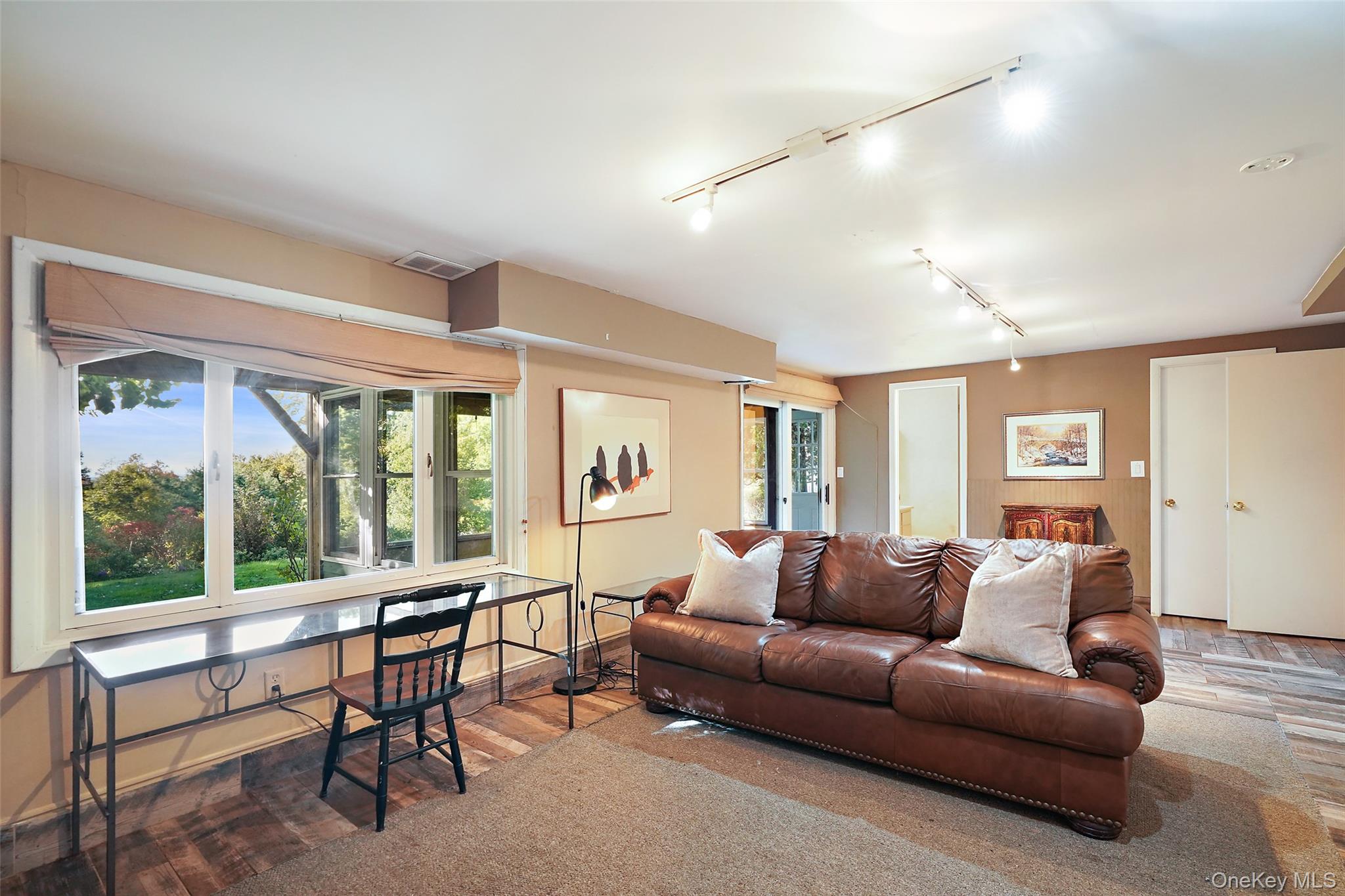 Living room with a brown leather sofa, large windows, and views of trees and lawn.