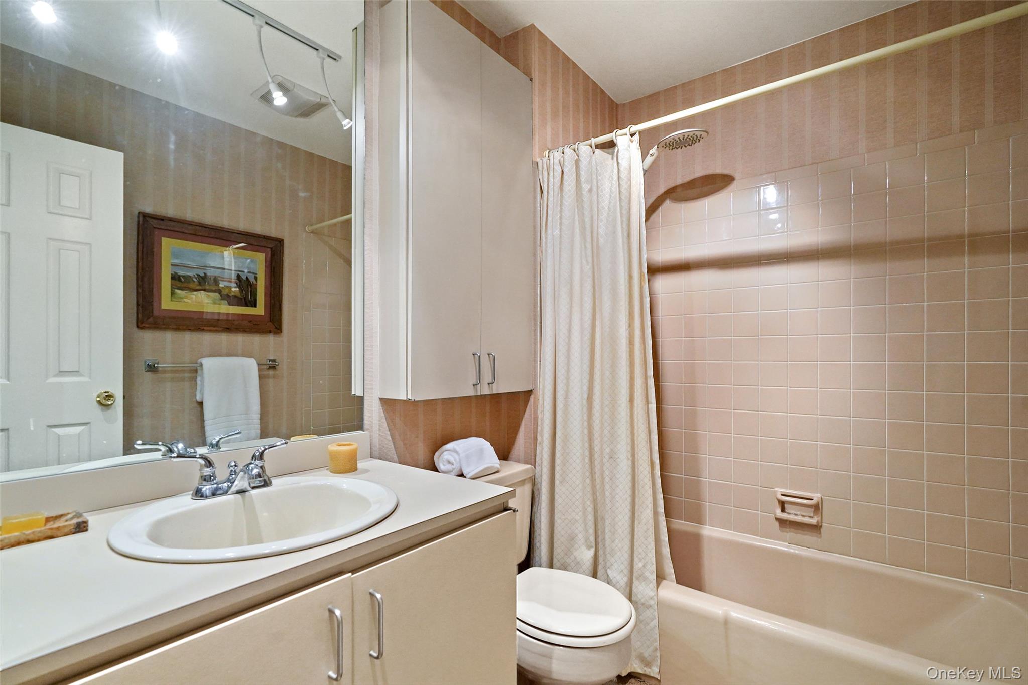 Bathroom with a white vanity, mirrored wall, and bathtub with dusty-pink tile.