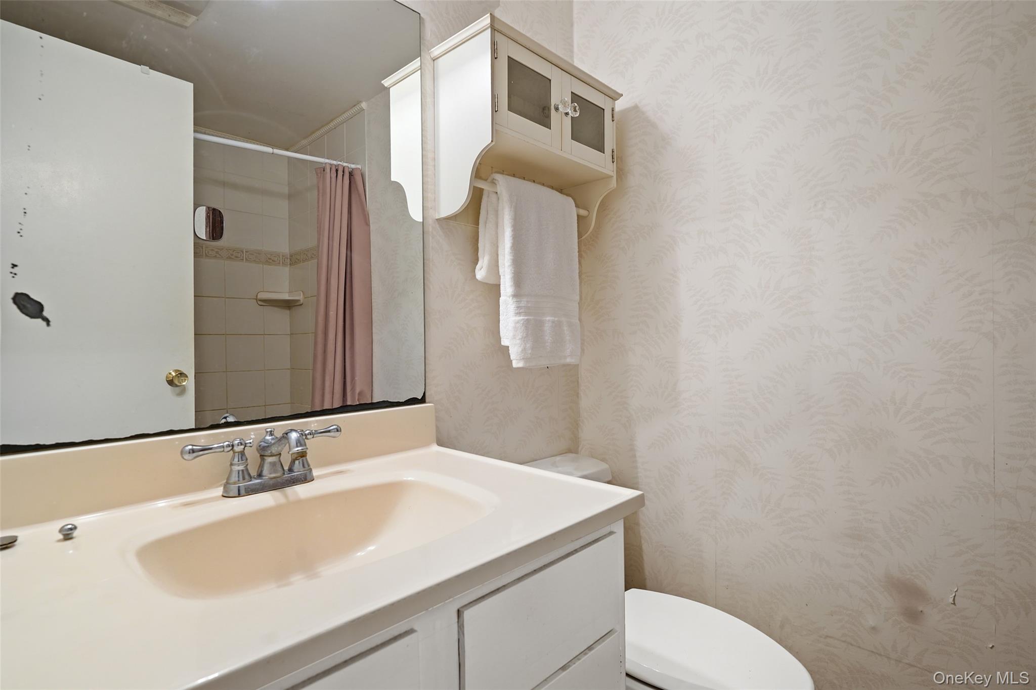 Bathroom vanity with cream sink, mirrored cabinet, and pink shower curtain.