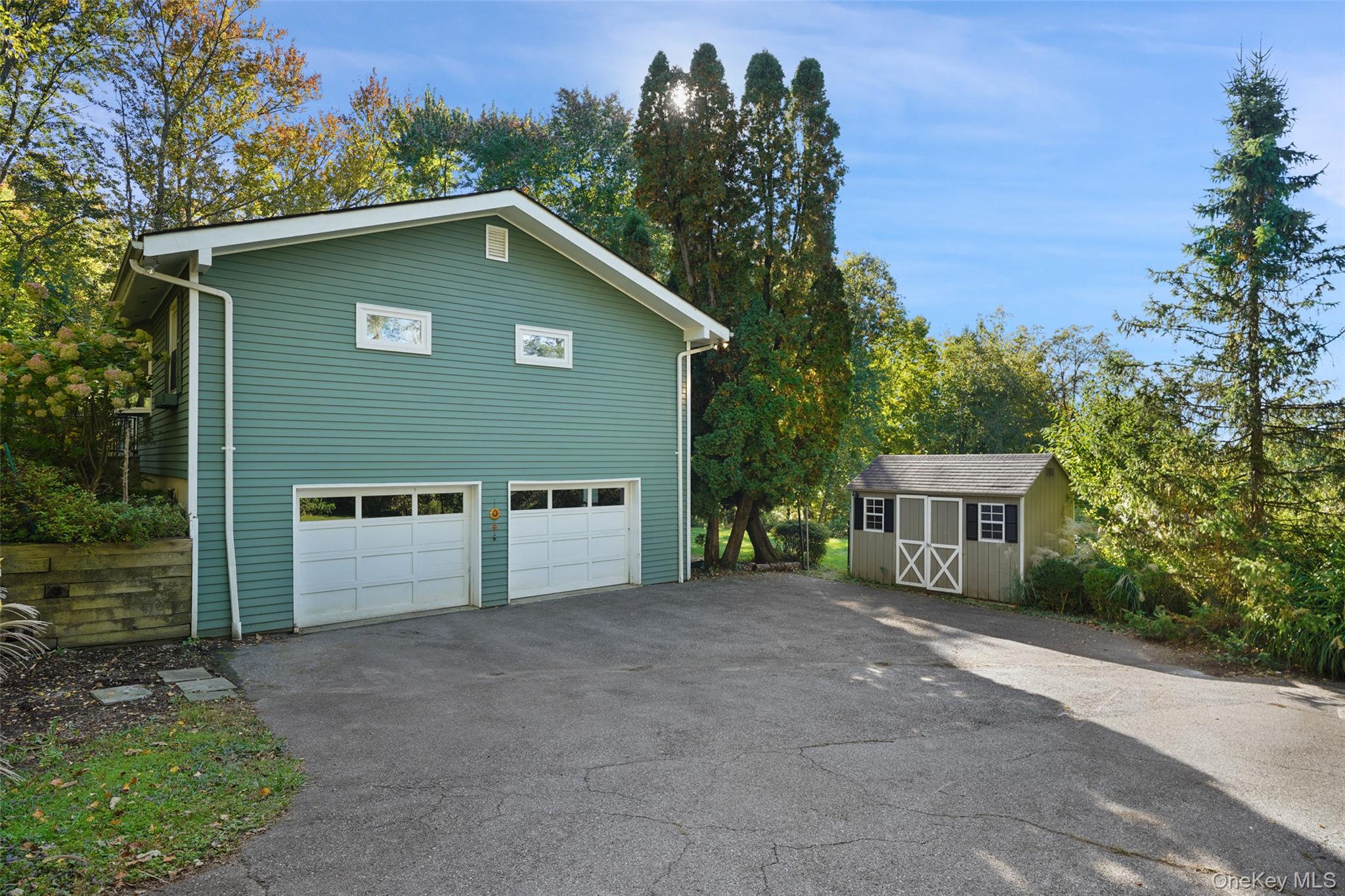 Teal-green detached garage with two white doors and a small shed beside the paved driveway.