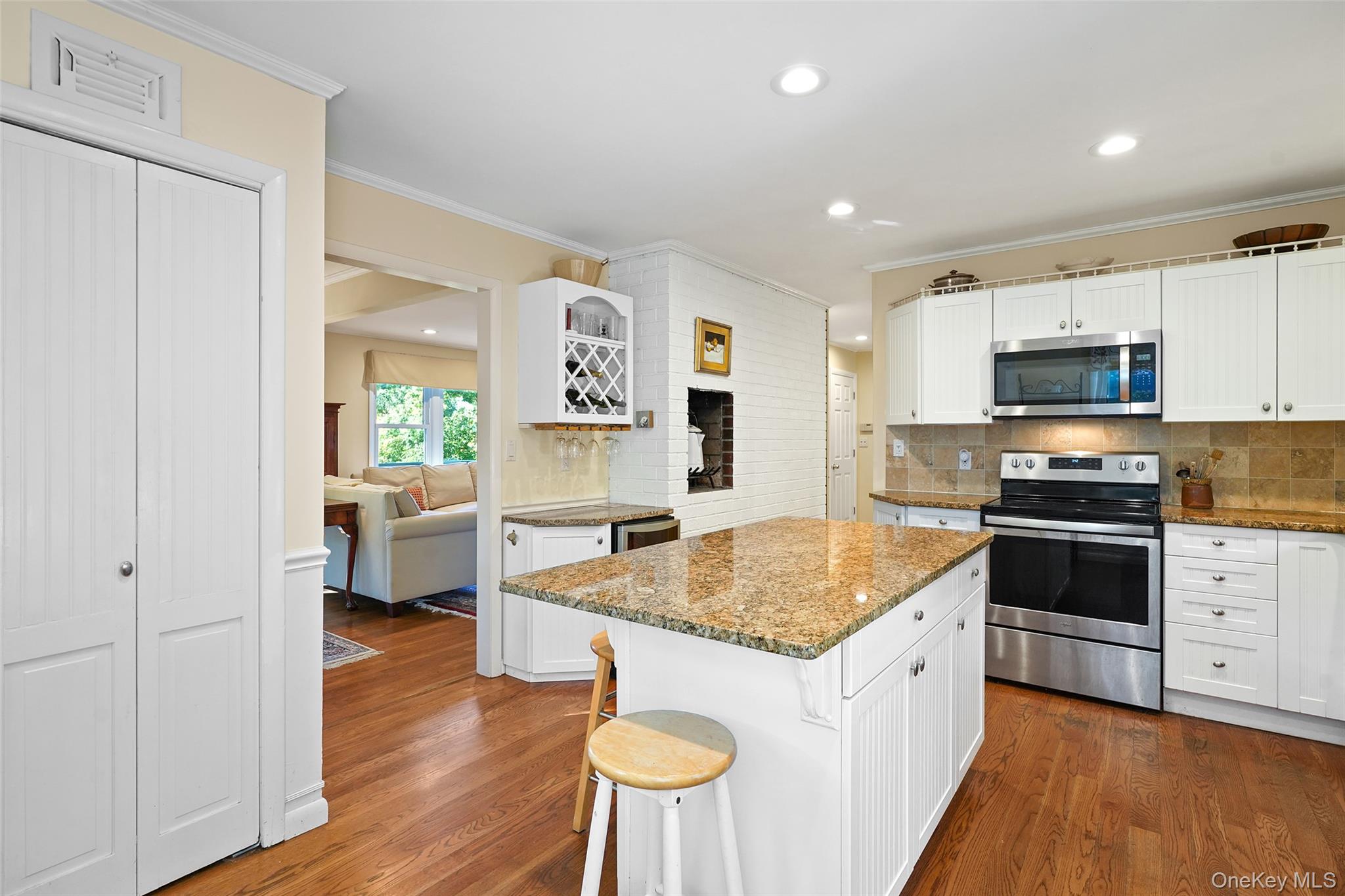 Kitchen with a large granite island, white cabinets, stainless steel appliances, and a brick fireplace.