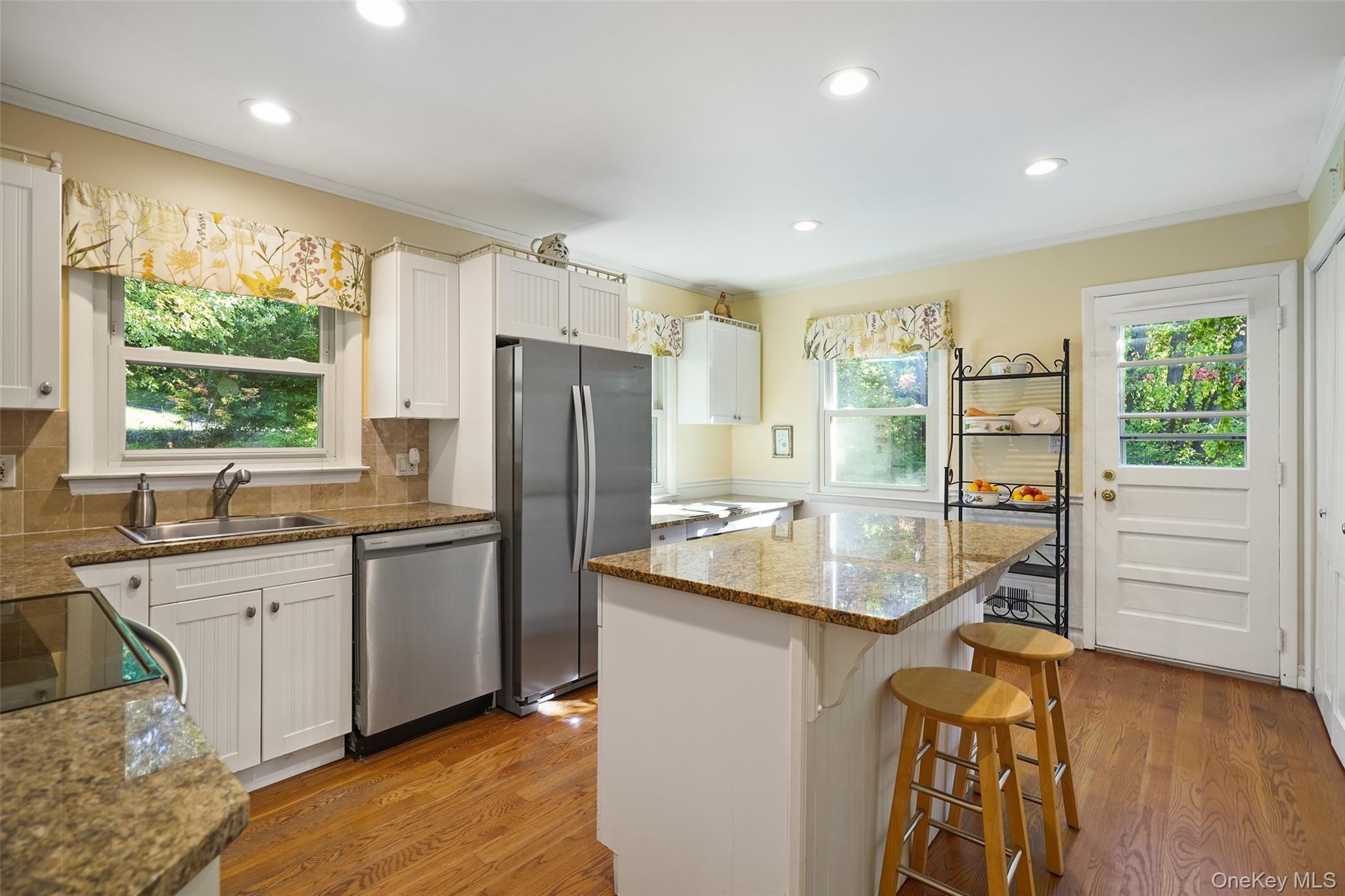 Kitchen with a granite island and stools, white cabinets, stainless steel appliances, and hardwood floors.