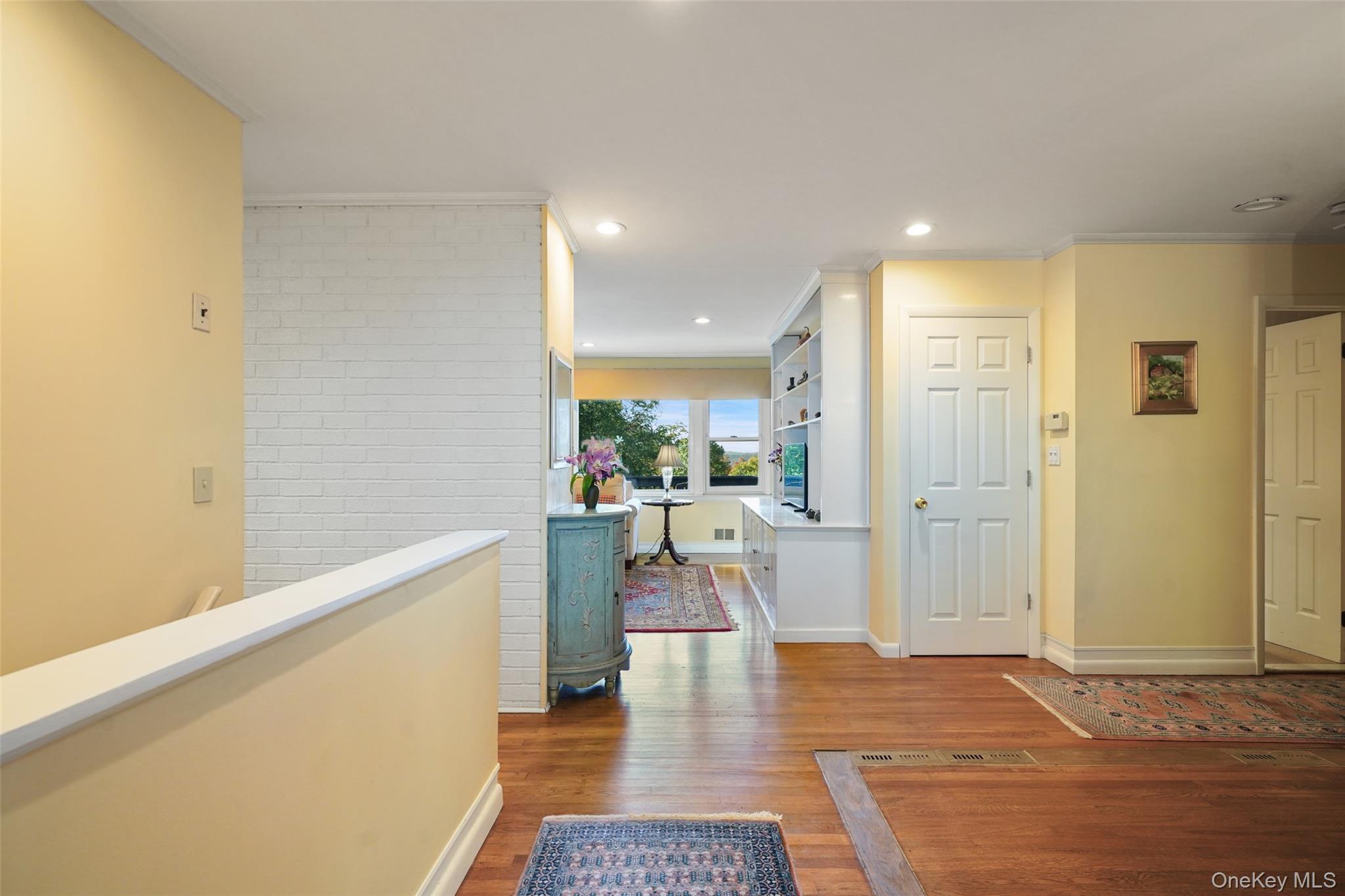 Hallway with hardwood floors, a white brick partition, patterned rugs, and a sitting area by the window.