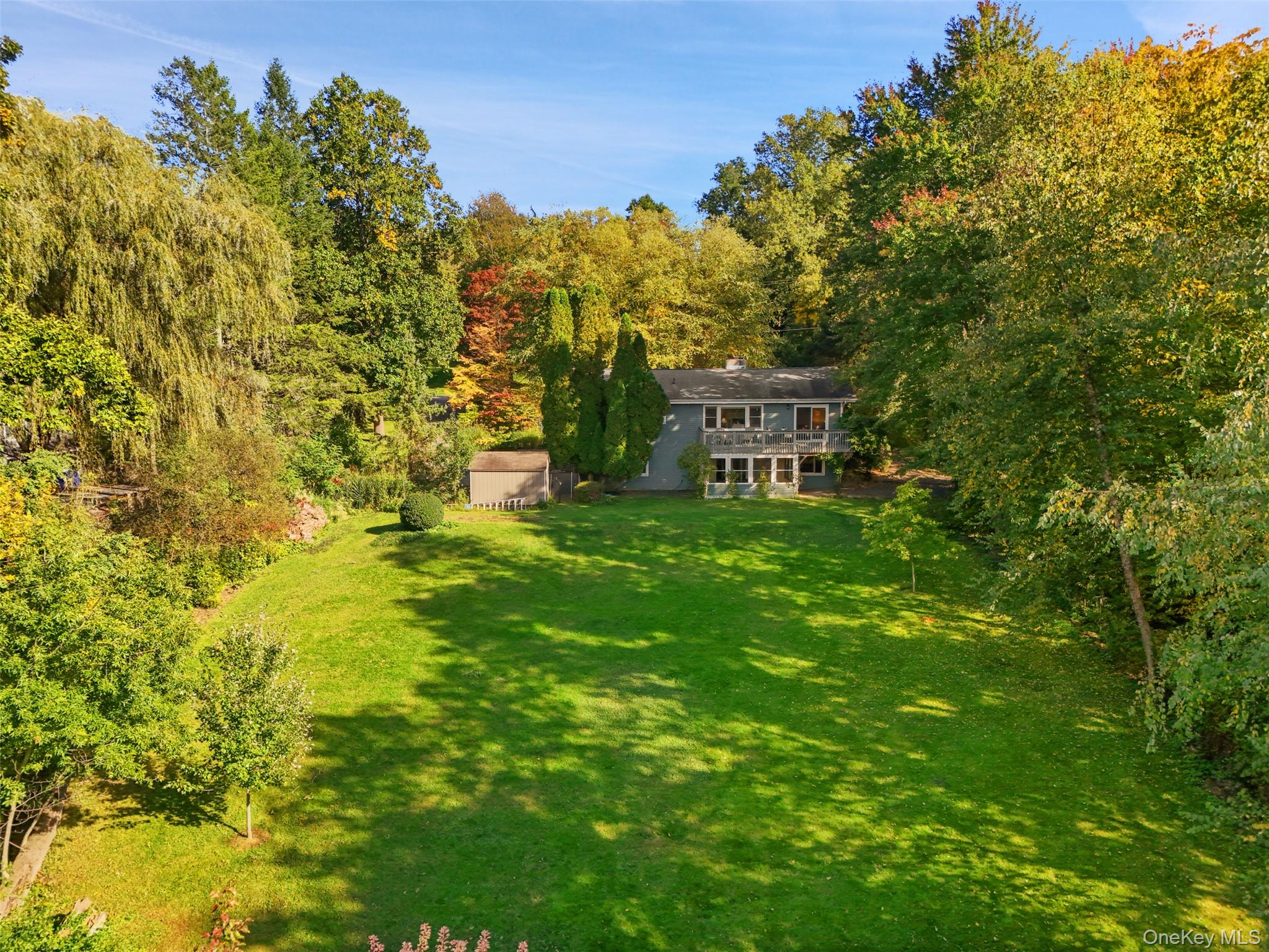 Home set beyond a broad lawn, framed by mature autumn trees, with a rear deck and small shed.
